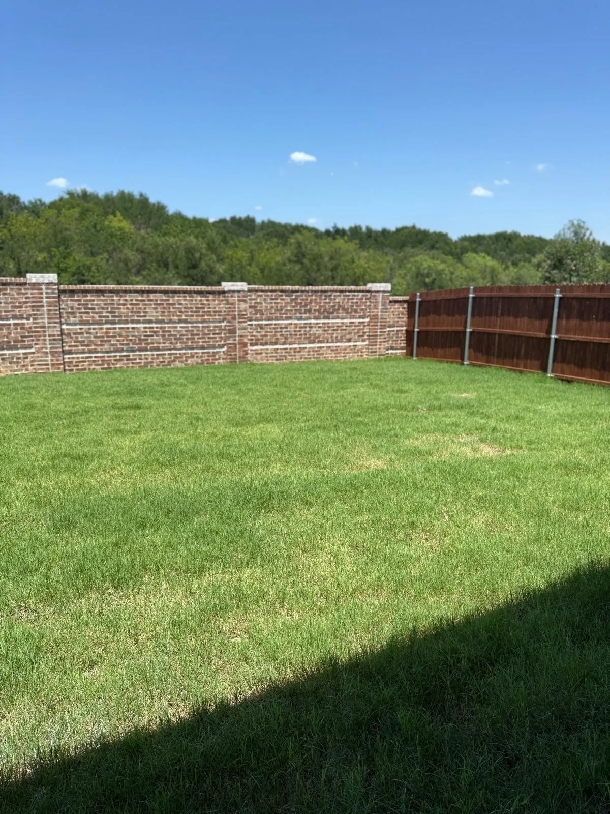 Backyard featuring a manicured lawn, brick perimeter wall with stone cap detail, and wood-slat fencing