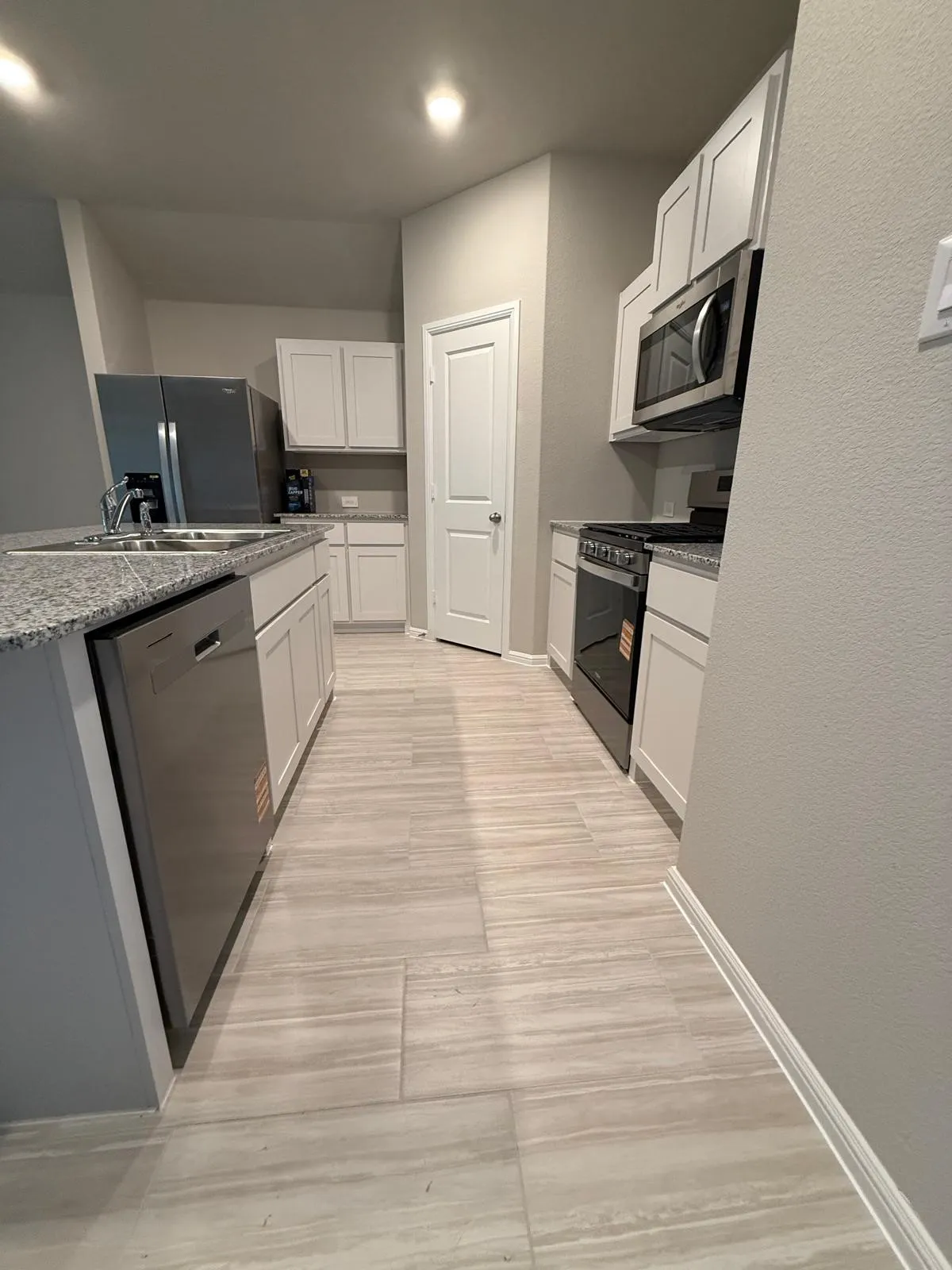 Kitchen featuring shaker-style white cabinetry, stone-finish countertops, stainless steel appliances, and large-format tile flooring