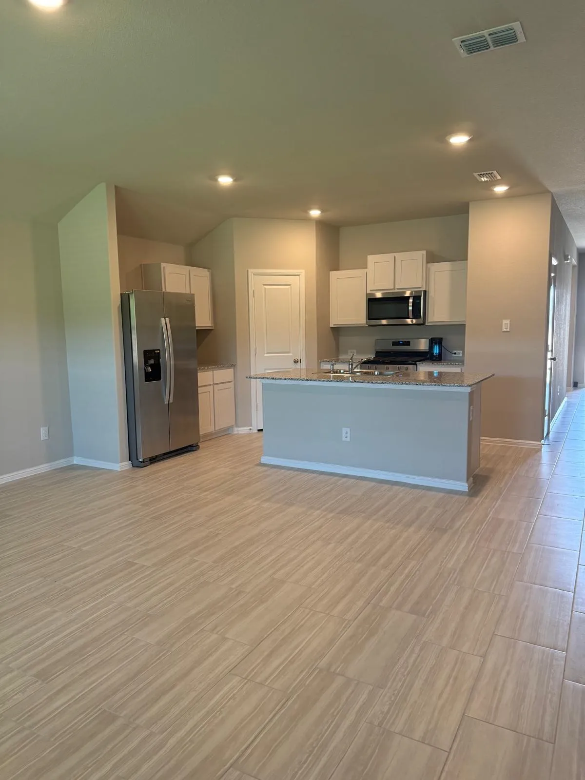 Kitchen featuring a central island with stone-style countertops, stainless steel appliances, white cabinetry, and wood-finish tile flooring