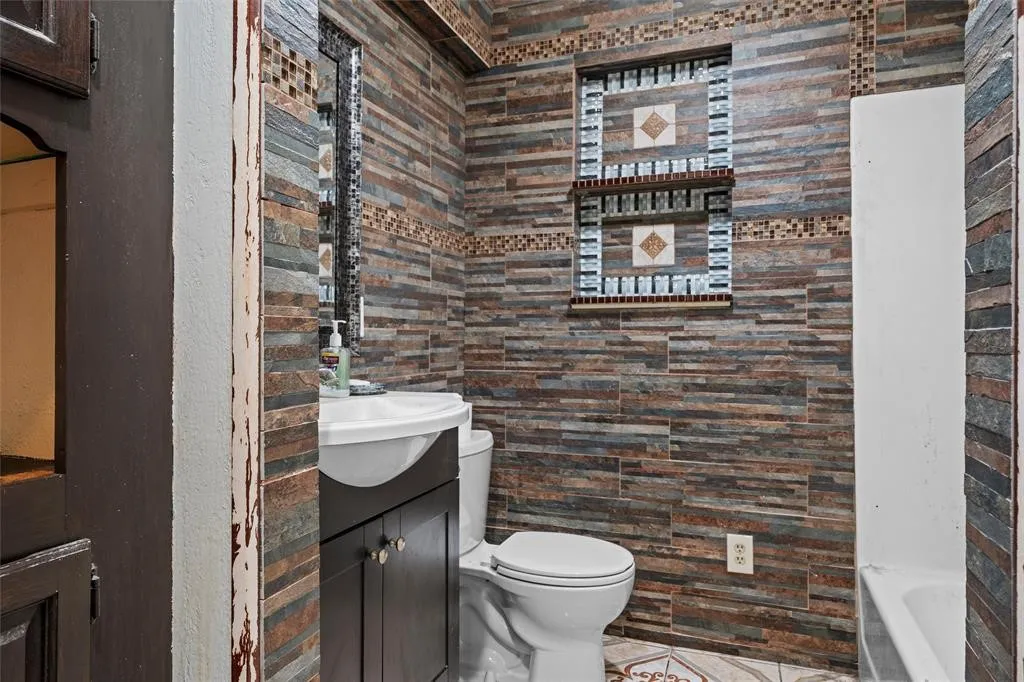 Bathroom featuring full-height stacked stone wall cladding, built-in tiled recessed shelving, dark wood-finish cabinetry, and ceramic tile flooring