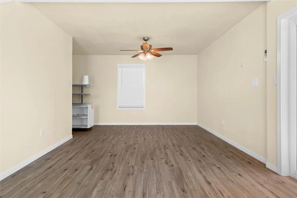 Neutral-toned room featuring wood-finish flooring, a single window with blinds, and a ceiling-mounted fan with integrated lighting