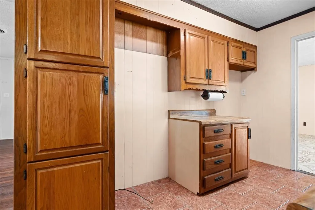 Kitchen area featuring wood cabinetry, laminate countertops, tile flooring, and integrated wall-mounted storage