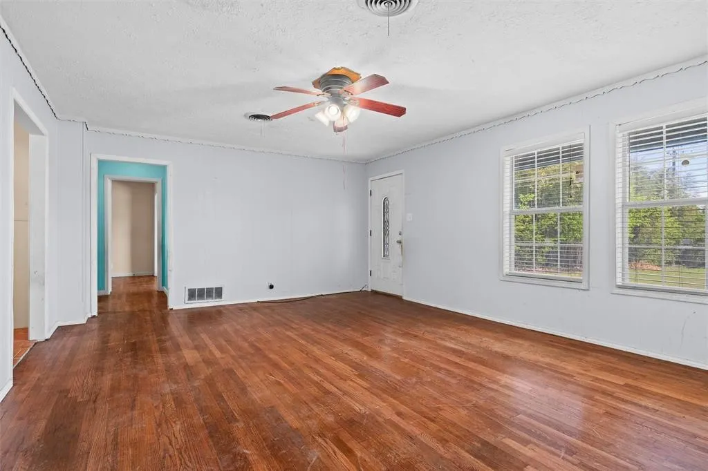 Living area featuring wood-finish flooring, dual windows with blinds, a central ceiling fan with integrated lighting, and a glass-paneled exterior door