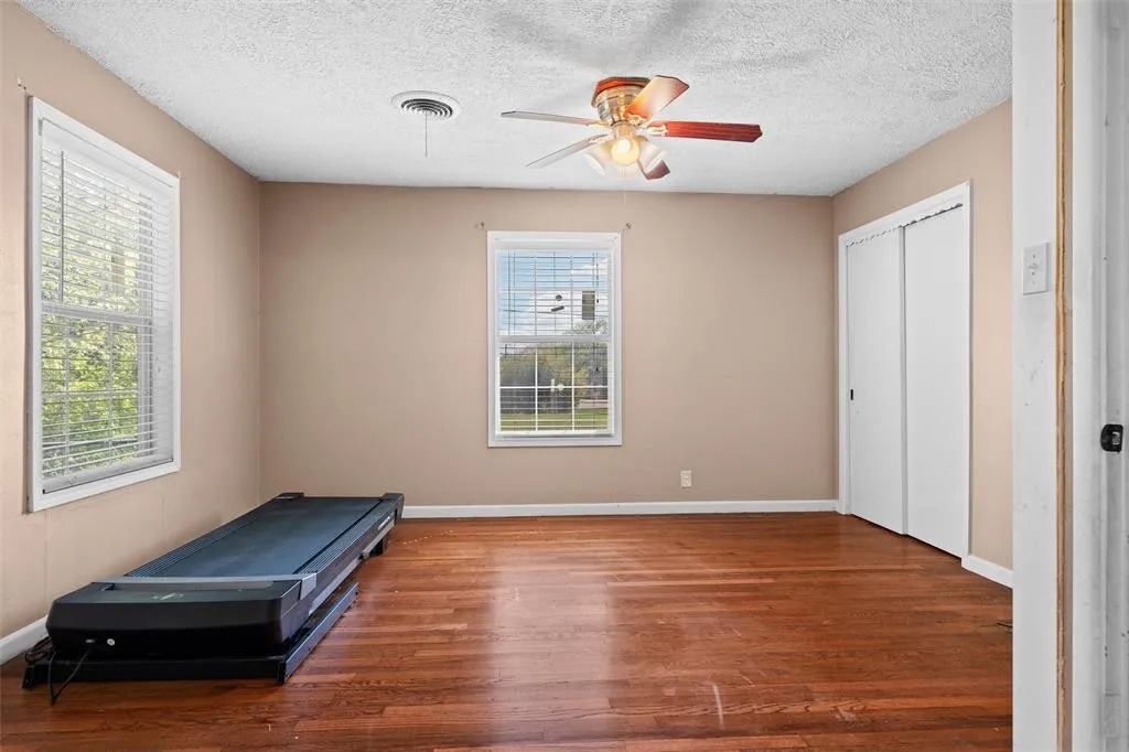 Room featuring wood-finish flooring, two windows with horizontal blinds, a ceiling fan with integrated lighting, and a closet with sliding doors