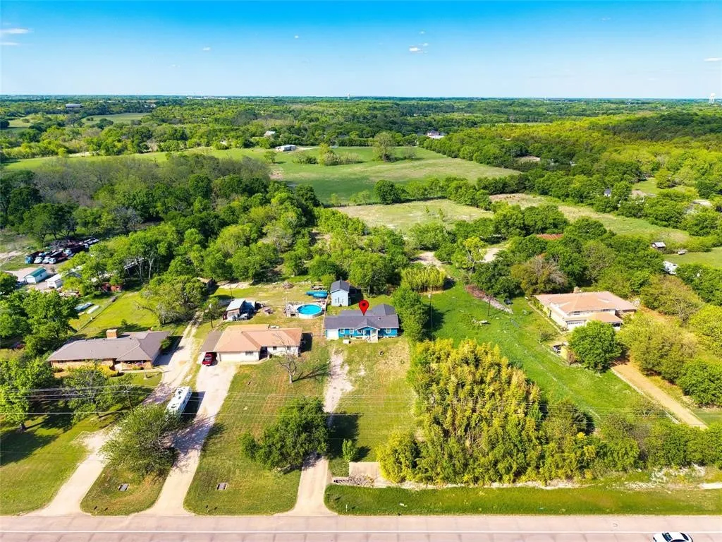 Aerial perspective of a property featuring extensive acreage, mature trees, and a paved road frontage