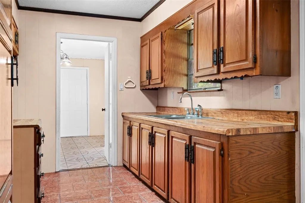 Kitchen featuring wood cabinetry, integrated wood-finish countertops, stainless steel sink with metal fixtures, and ceramic tile flooring