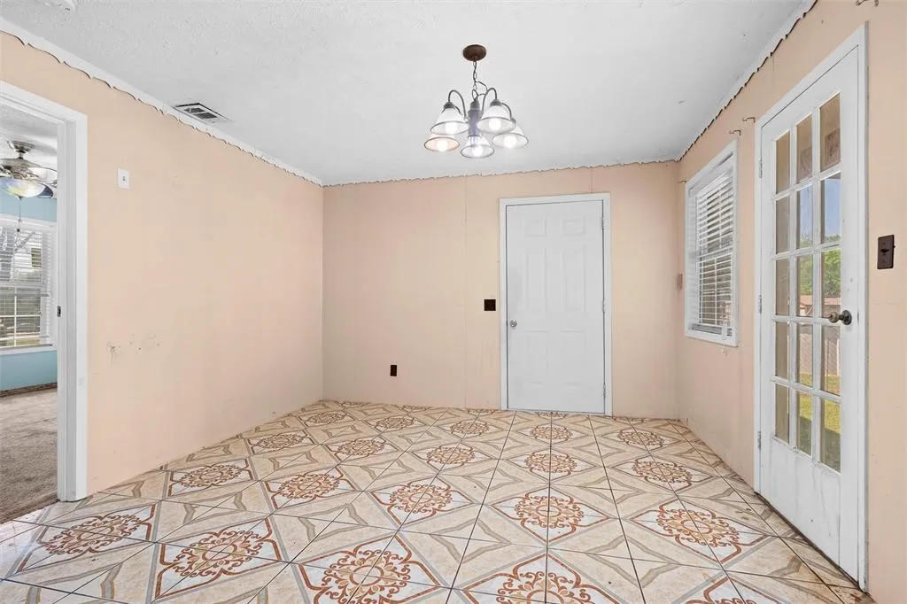 Room featuring patterned tile flooring, a multi-light chandelier, a glass-paneled exterior door, and a six-panel interior door