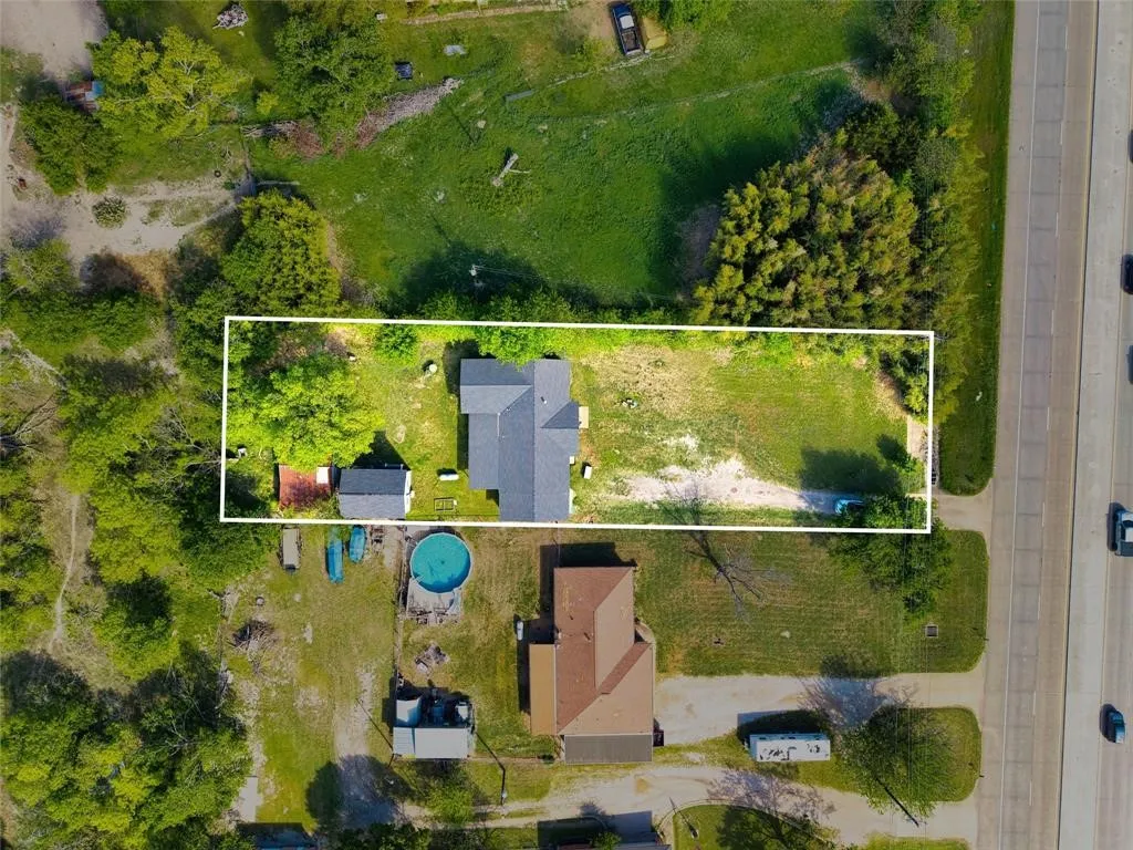 Aerial view of a rectangular lot featuring a detached residence, a secondary outbuilding, mature tree canopy, and open grounds