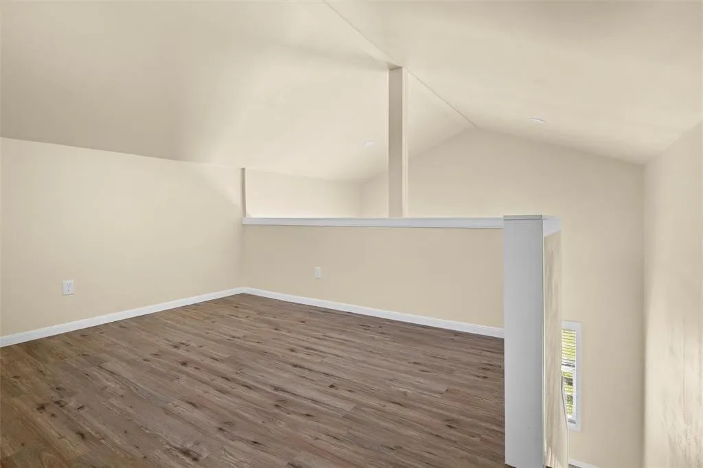 Vaulted ceiling, wood-finish flooring, and a white railing featuring a central support post
