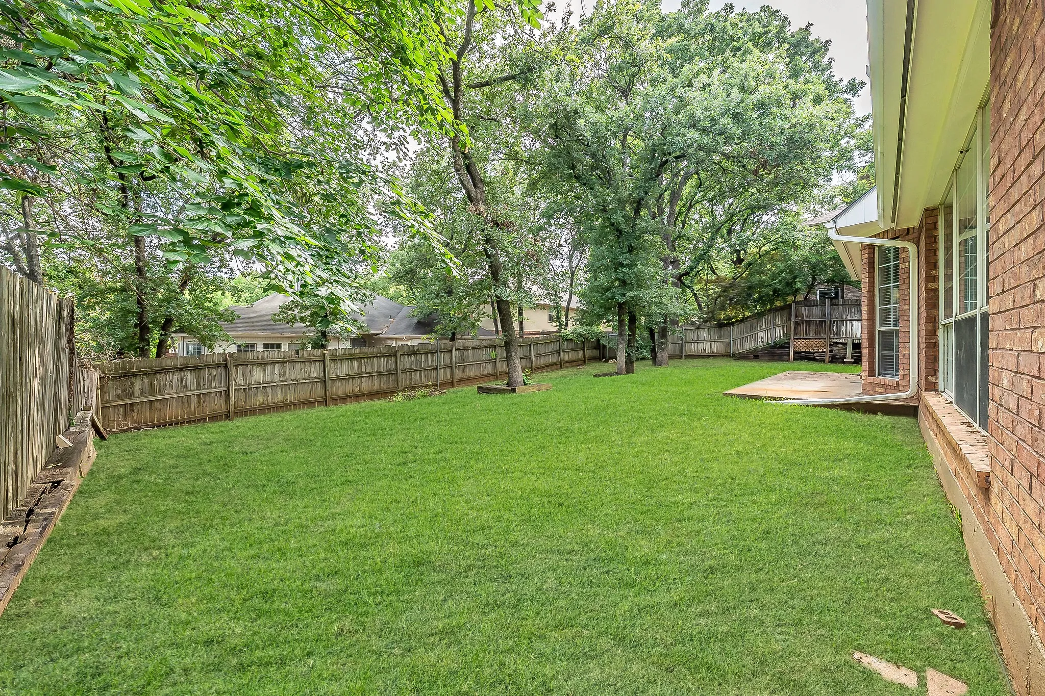 Backyard with shade trees and wooden fence.