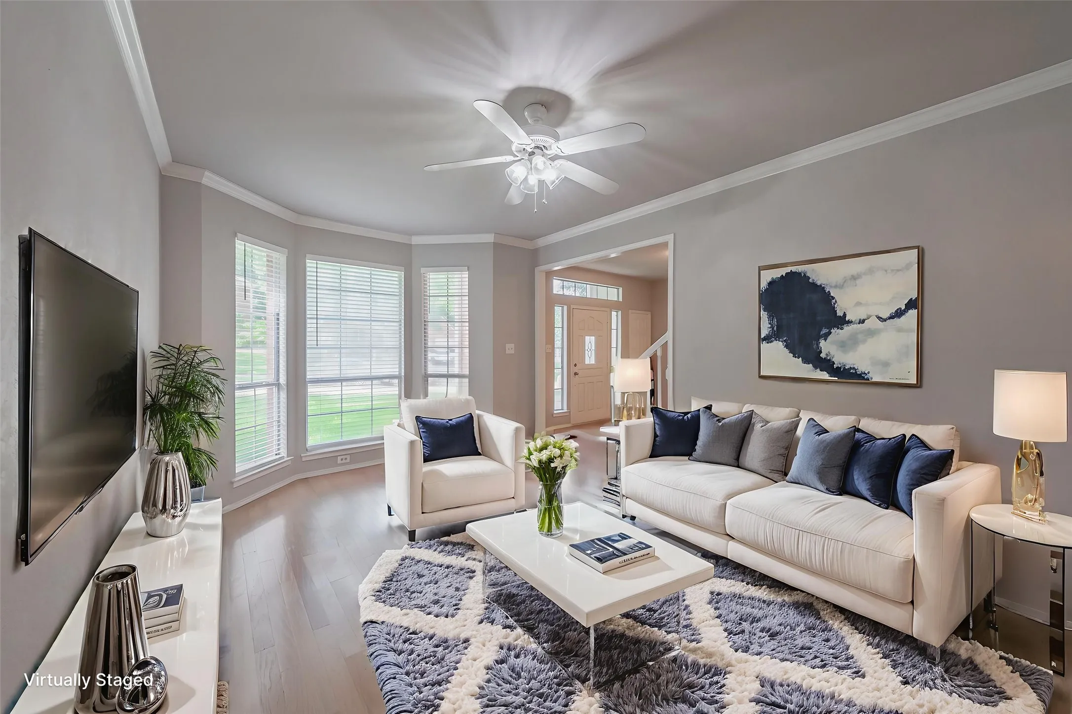 Virtually staged living room featuring beautiful hardwood floors, crown molding, a bay window, and a ceiling fan for added comfort.
