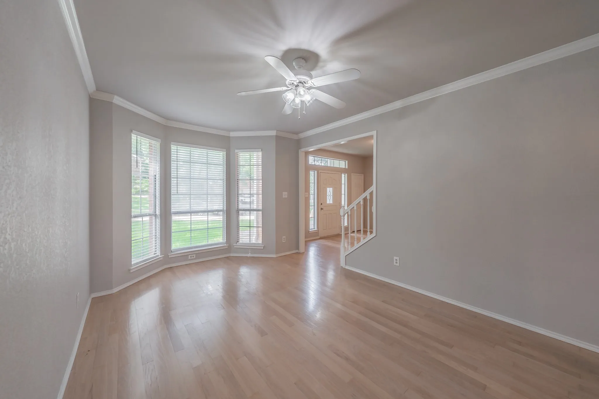Bright and spacious living room showcasing gleaming hardwood floors, abundant natural light from bay window, and crown molding.