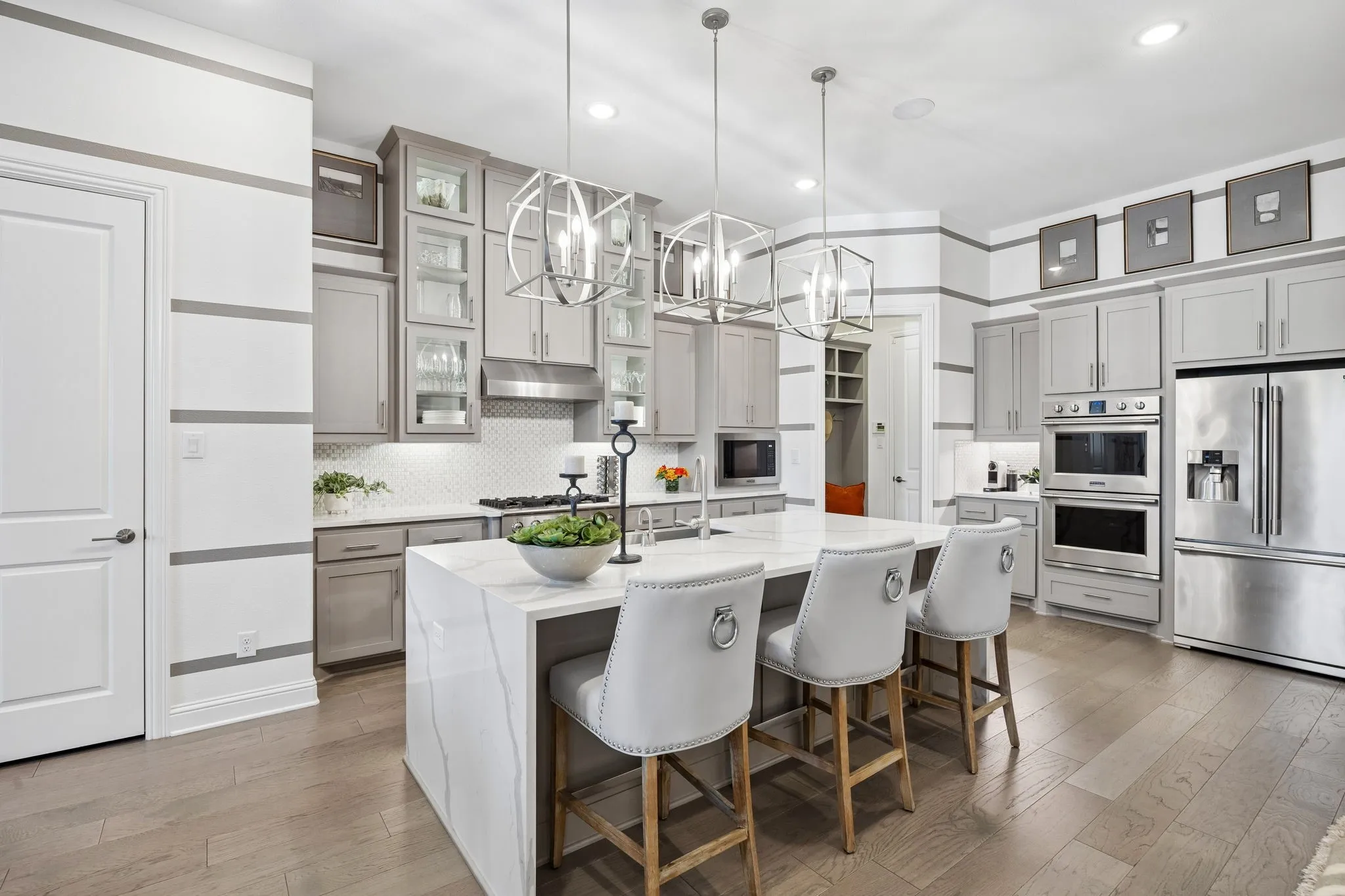 Stunning gourmet kitchen offers double ovens, waterfall edge Quartz Island, lit cabinets, 6 burner high end cooktop.