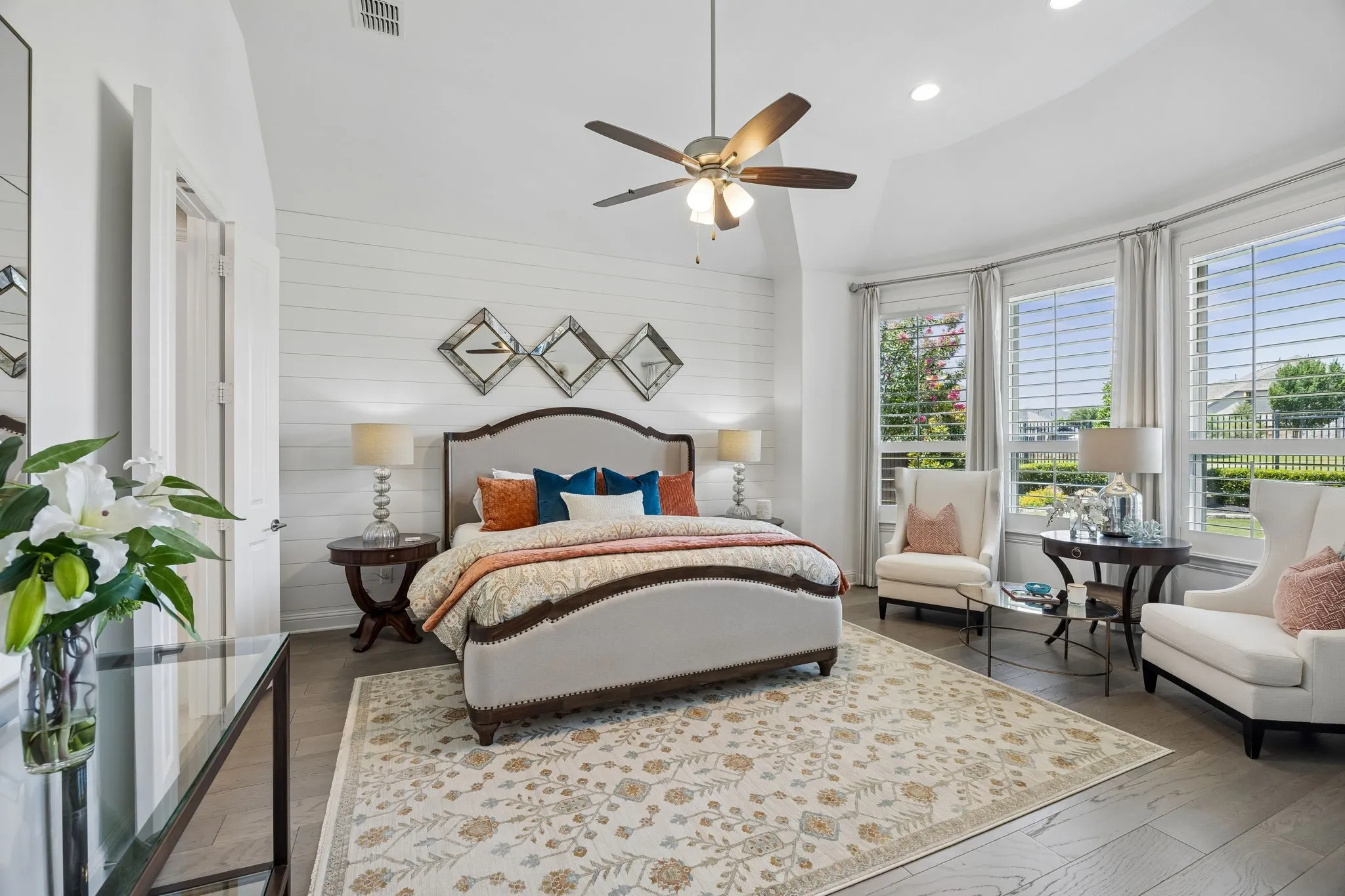 Large oversized primary bedroom boasts a striking wood accent wall, large bay window providing an abundance of natural light and stunning views across the lake and up the rolling hills of the greenbelt with towering trees.