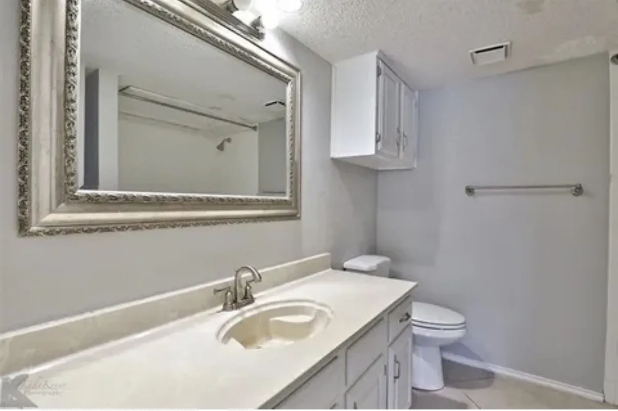 Bathroom featuring a vanity with integrated sink, stone-finish countertop, white cabinetry, wall-mounted mirror, and overhead lighting