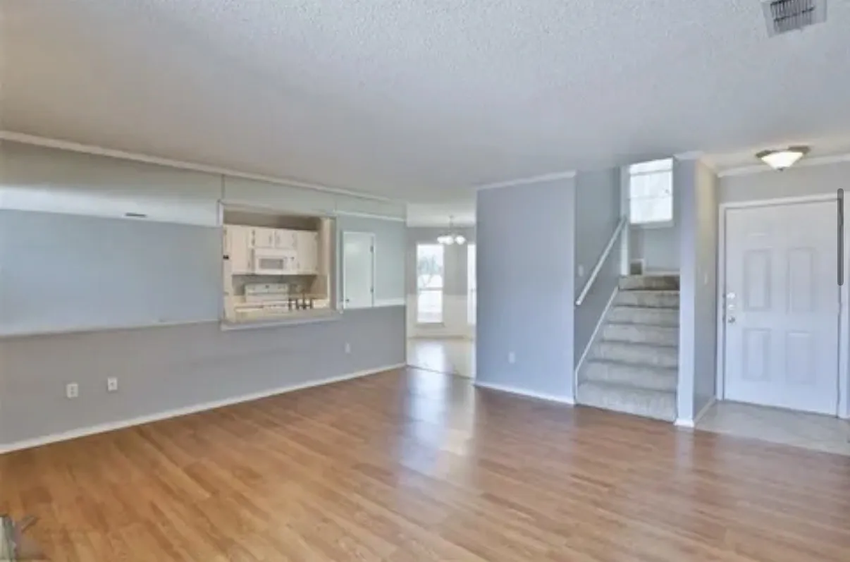 Open floor plan featuring wood-finish flooring, a pass-through wall cutout, staircase with a white handrail, and a paneled entry door
