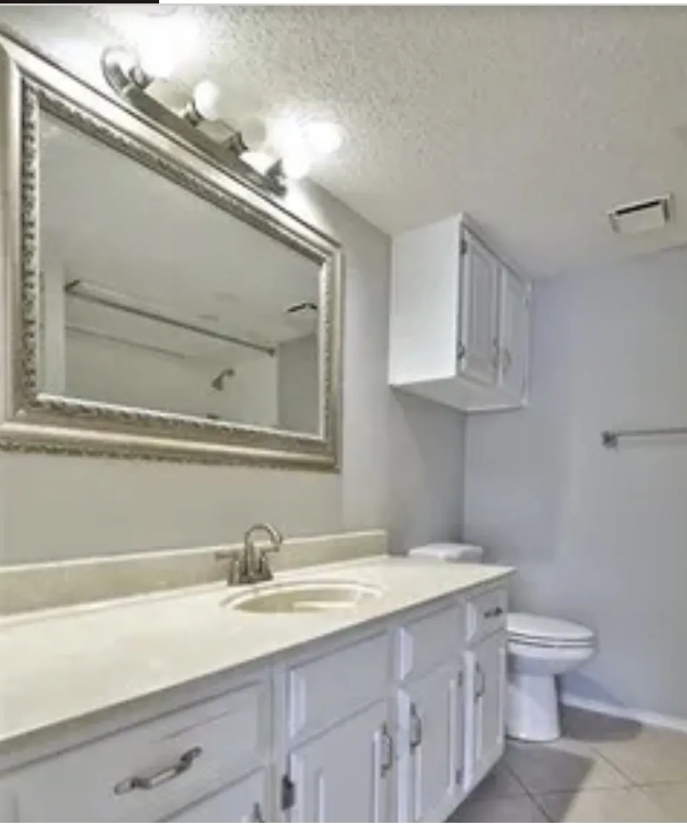 White vanity with integrated countertop and sink, polished chrome faucet, framed wall mirror, overhead vanity lighting, and wall-mounted storage cabinetry