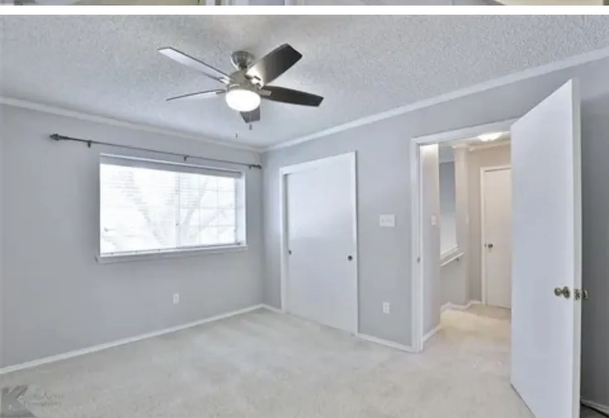Neutral-toned interior featuring wall-to-wall carpeting, a multi-blade ceiling fan with integrated lighting, a single-hung window with a curtain rod, and white interior doors