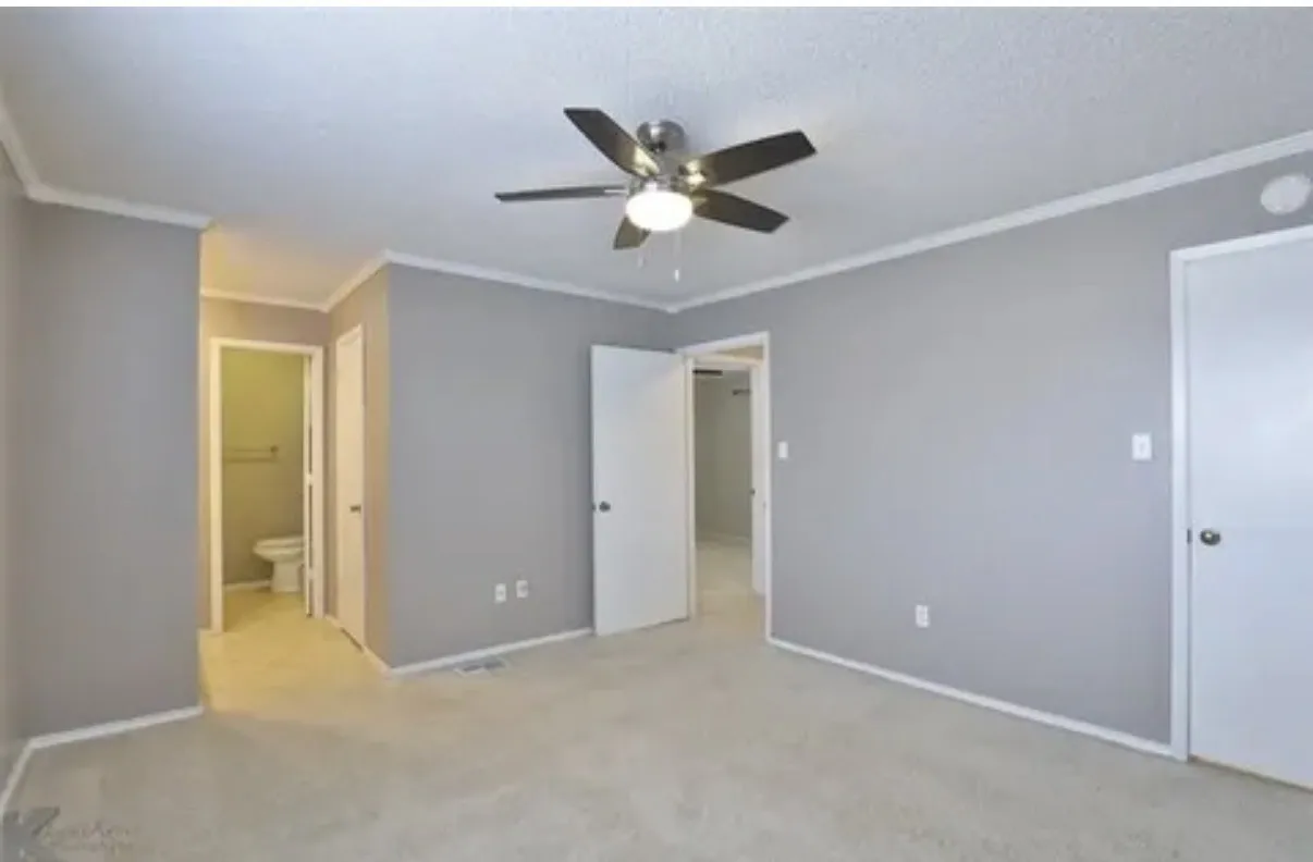 Neutral-toned interior featuring wall-to-wall carpeting, a multi-blade ceiling fan with integrated lighting, and solid-core interior doors