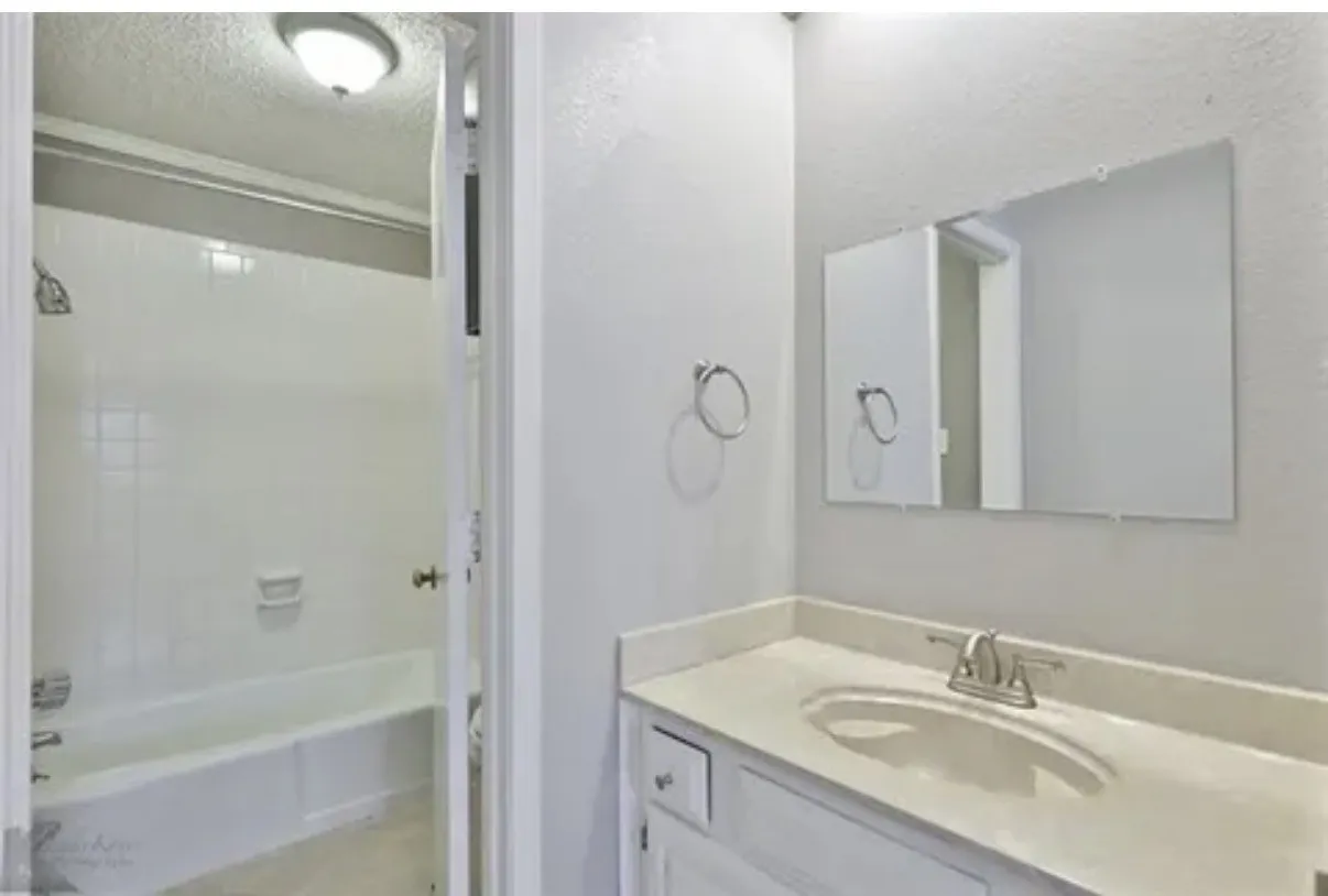 Vanity featuring a solid surface countertop, undermount sink, chrome faucet, wall-mounted mirror, and white cabinetry