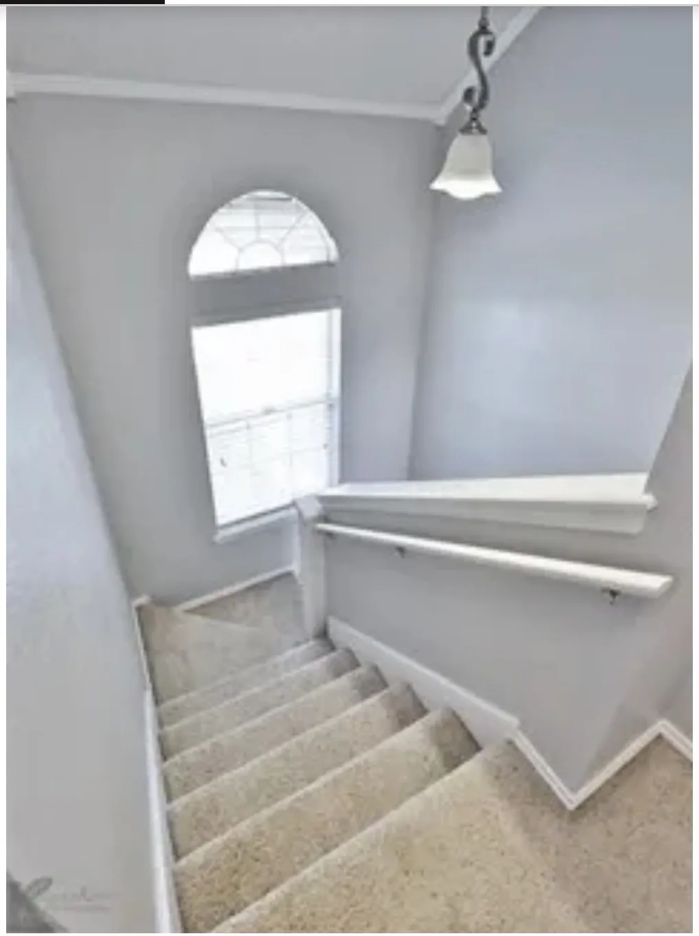 Staircase featuring neutral carpeting, a white railing, an arched window, and a hanging pendant light