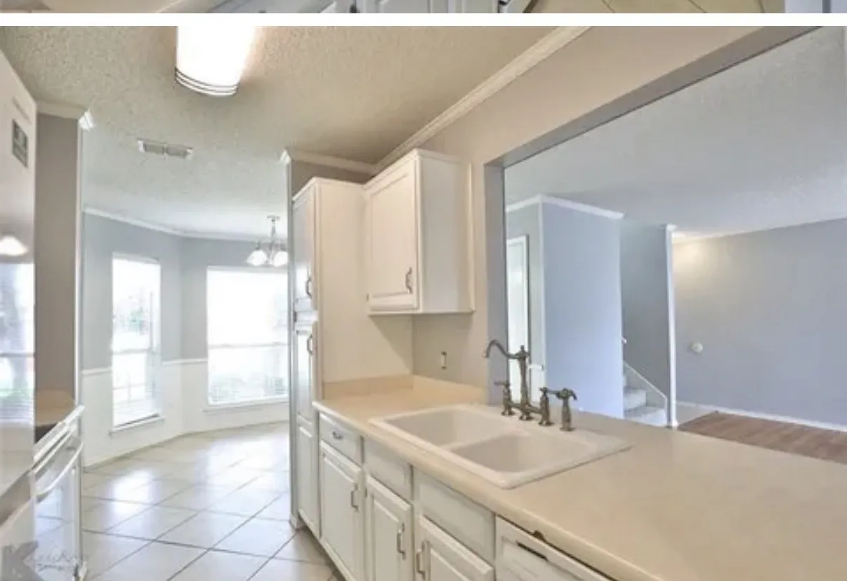 Kitchen featuring white cabinetry, solid-surface countertops, a double-basin sink with a gooseneck faucet, tile flooring, and a large pass-through window