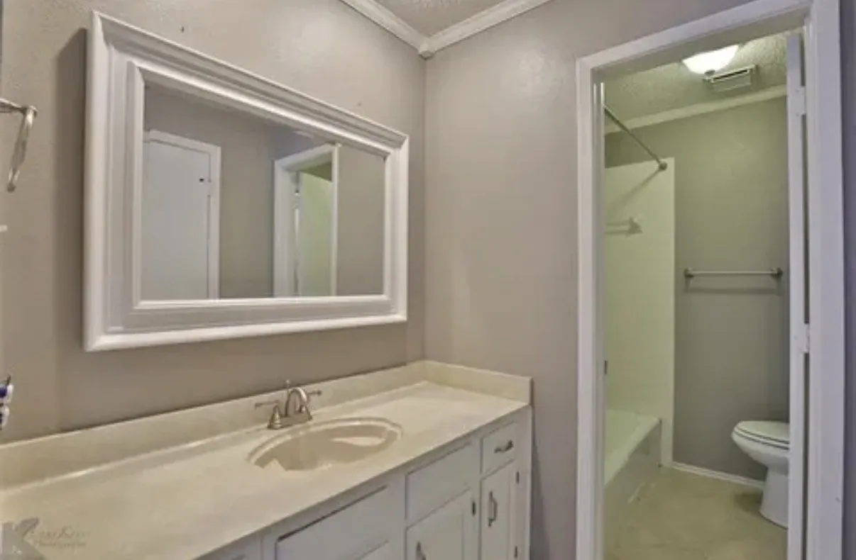 Bathroom featuring a white vanity with an integrated countertop, a wide-frame wall mirror, and a tub-shower combination with a surround