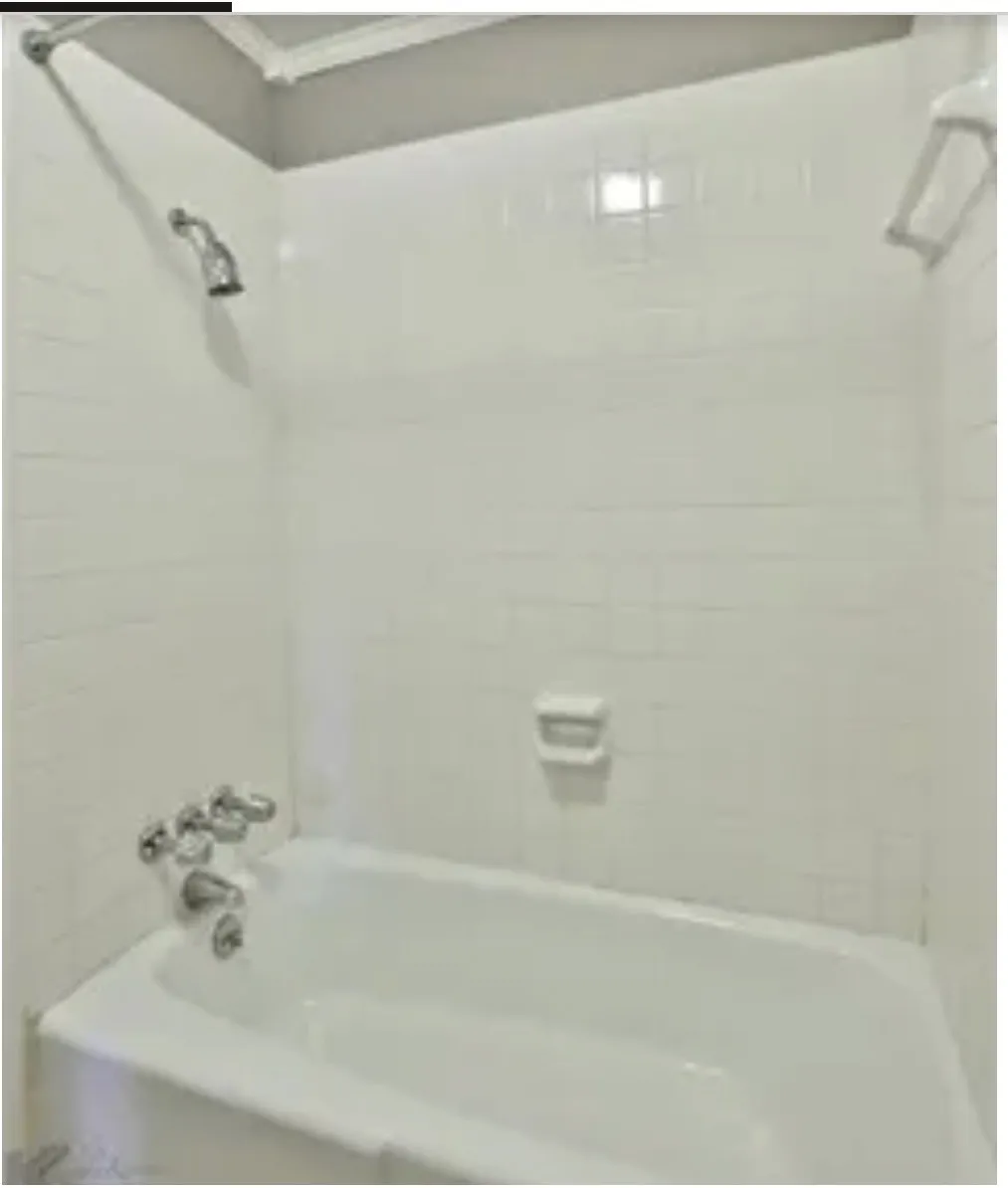 Bathtub enclosure featuring white ceramic wall tiles, a built-in recessed soap dish, chrome faucet hardware, and a shower head