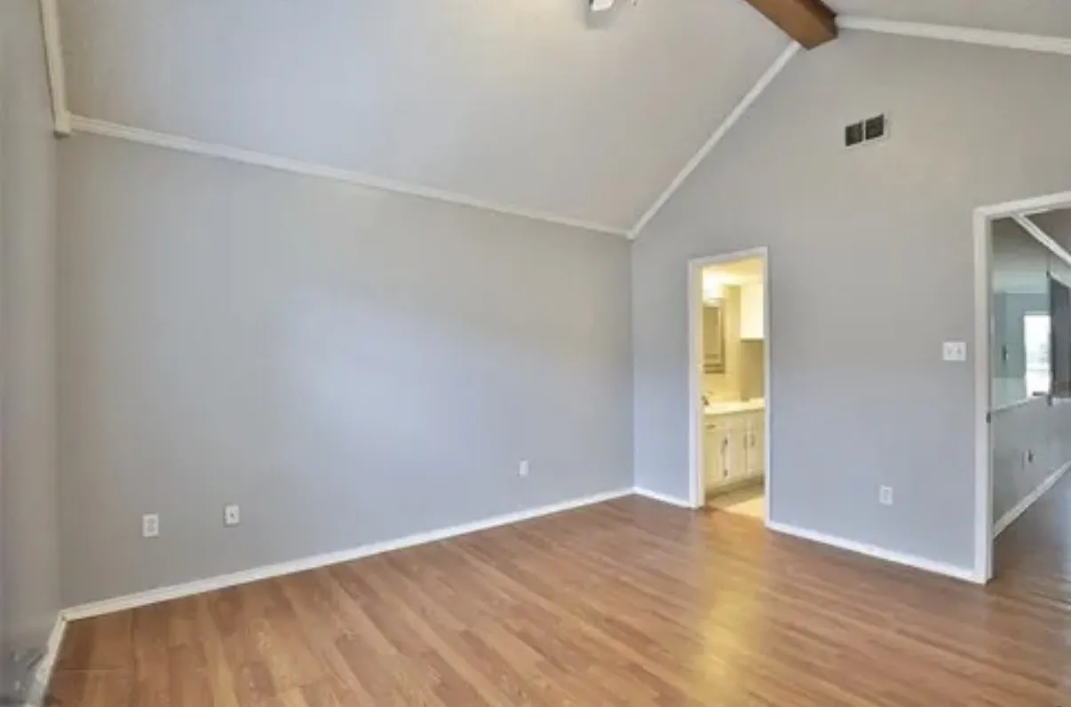 Vaulted ceiling featuring an exposed beam, wood-finish flooring, and neutral wall tones