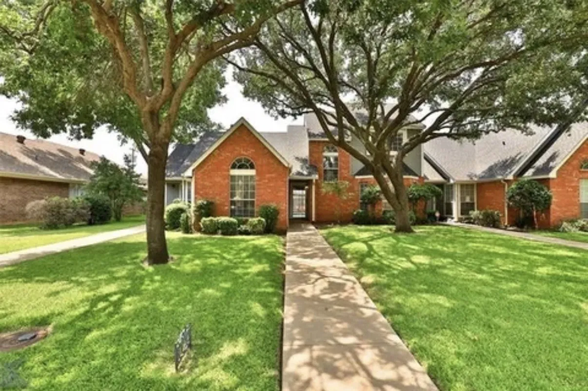 Brick exterior residence featuring a front gabled roofline, an arched window, a paved walkway, and mature trees on a landscaped lot