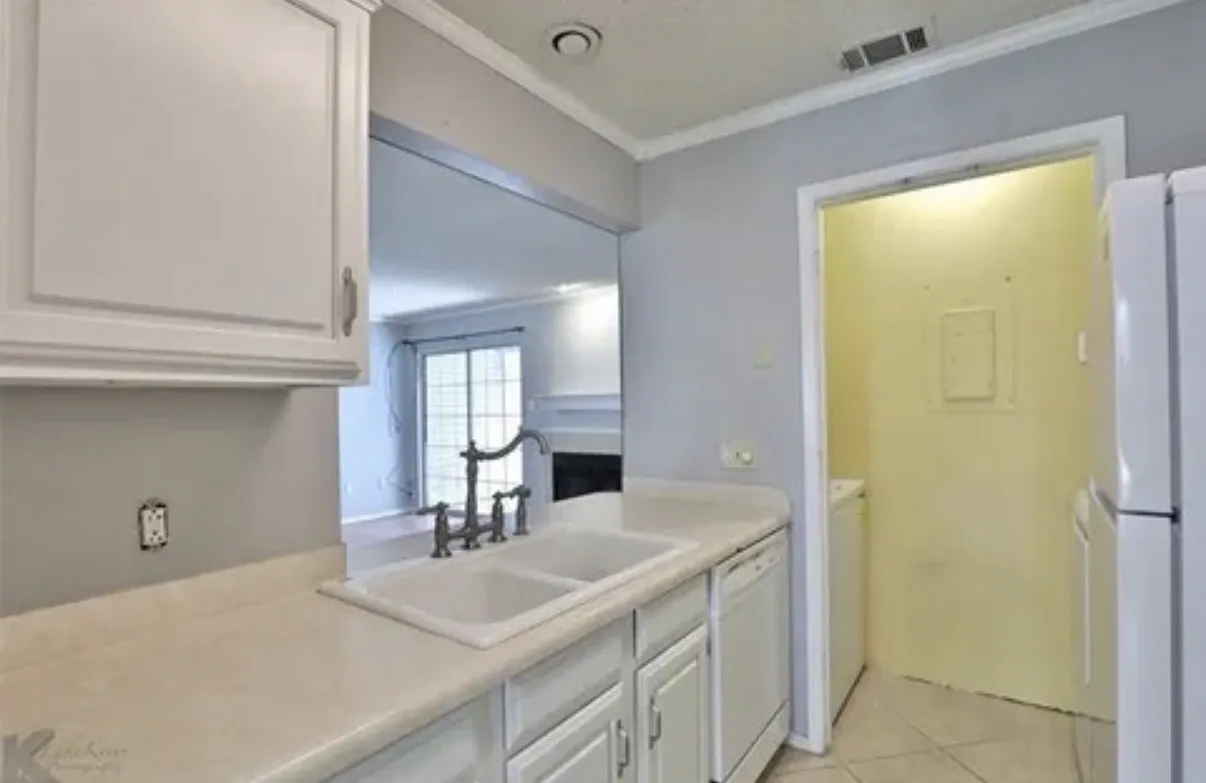 Kitchen featuring white cabinetry, solid-surface countertops, dual-basin drop-in sink with a high-arch faucet, integrated dishwasher, and tiled flooring