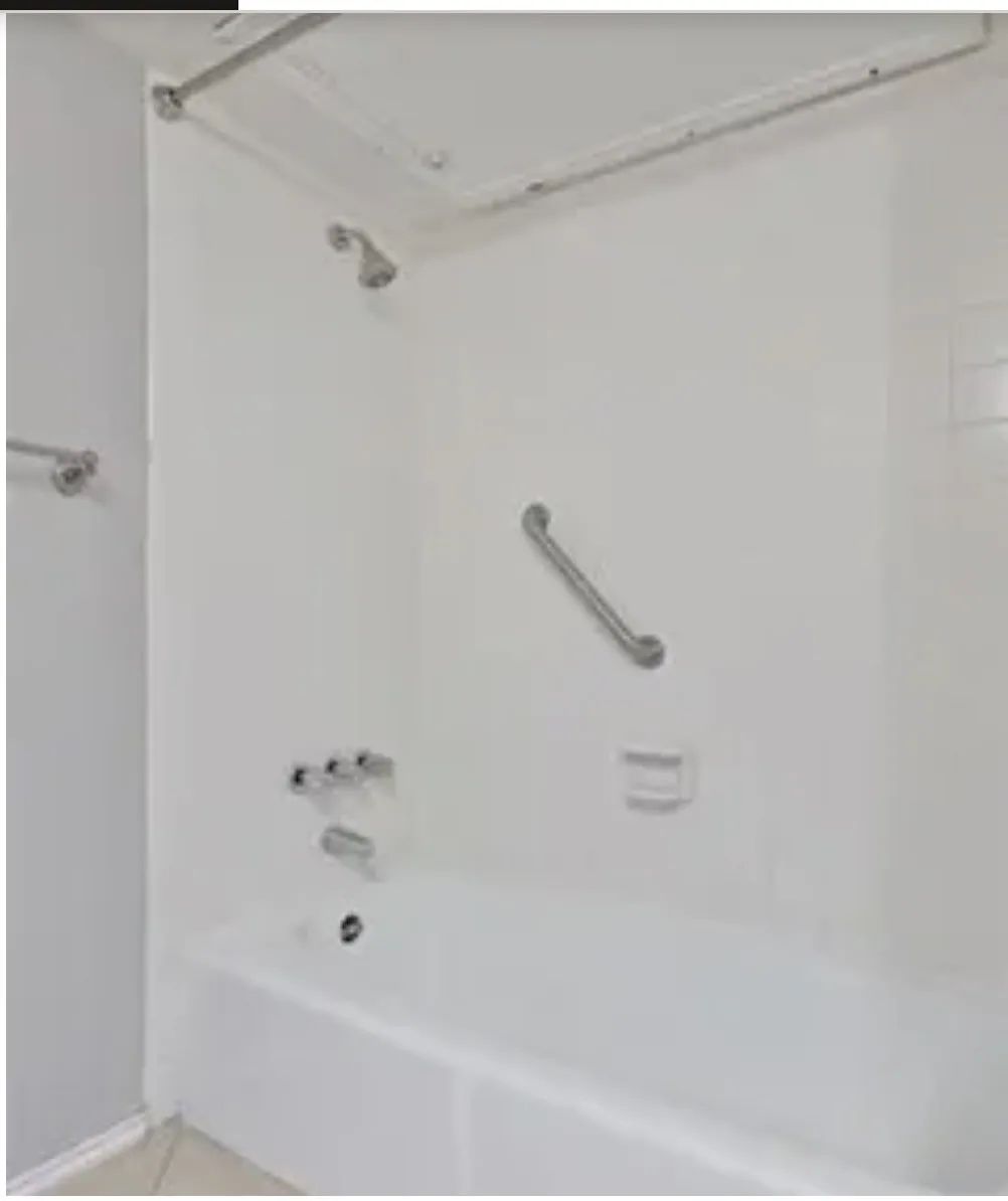 Bathtub surround featuring white wall panels, a metal showerhead, faucet hardware, an integrated soap dish, and a wall-mounted grab bar