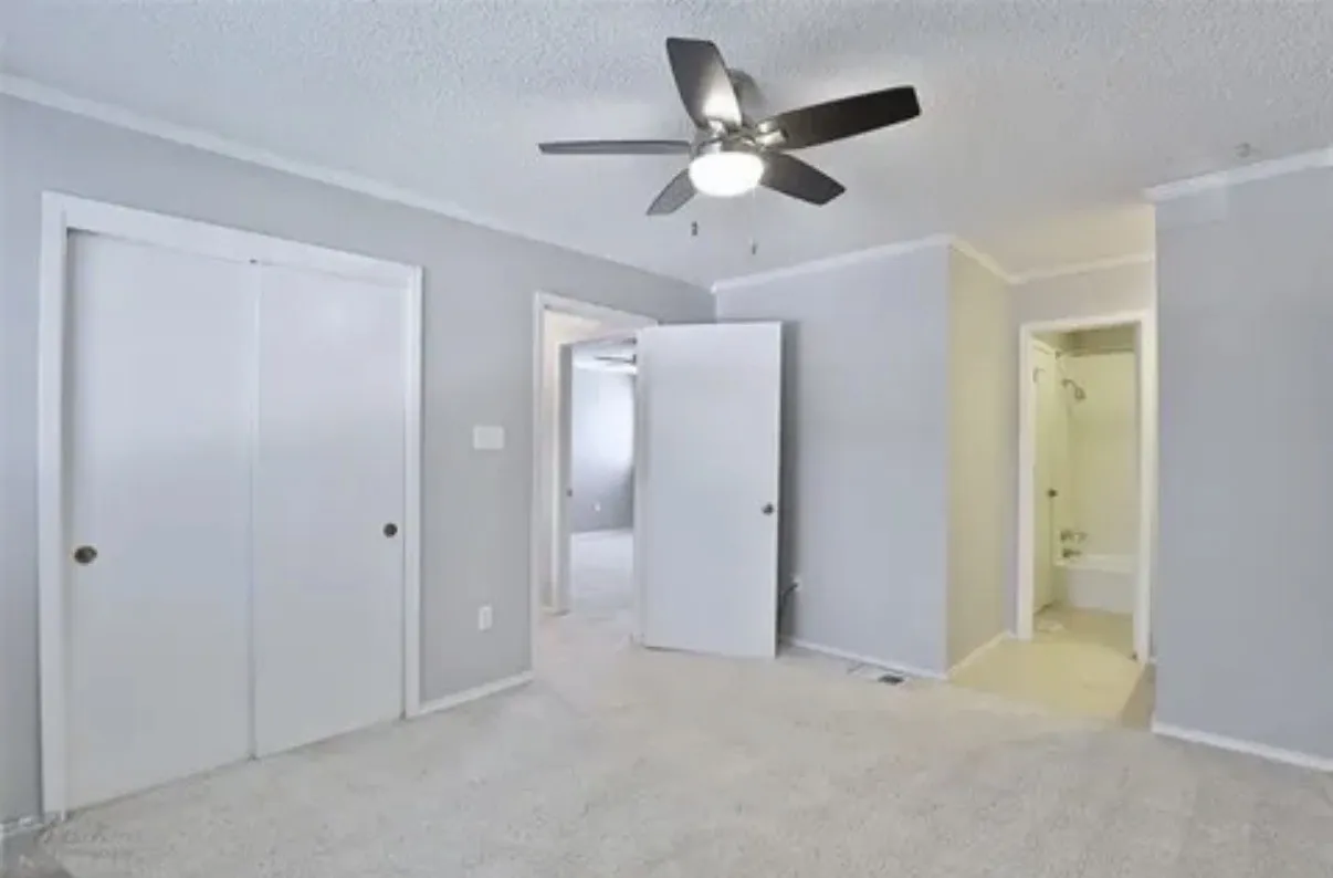 Interior room featuring neutral wall paint, wall-to-wall carpeting, a multi-blade ceiling fan with integrated lighting, and dual-panel closet doors