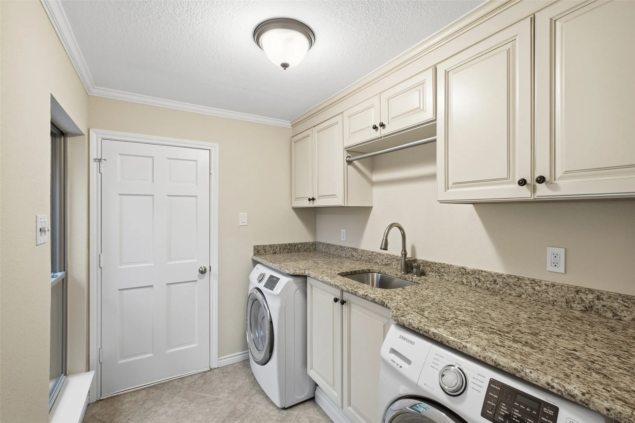 Laundry day made easy: granite counter, sink, raised-panel cabinetry and a hanging rod.