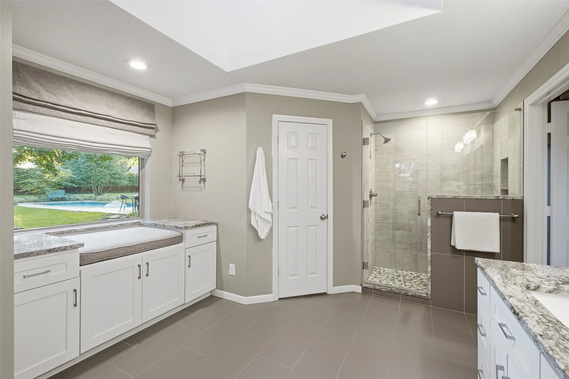 Frameless glass walk-in shower with pebble floor, plus a window seat overlooking the pool.