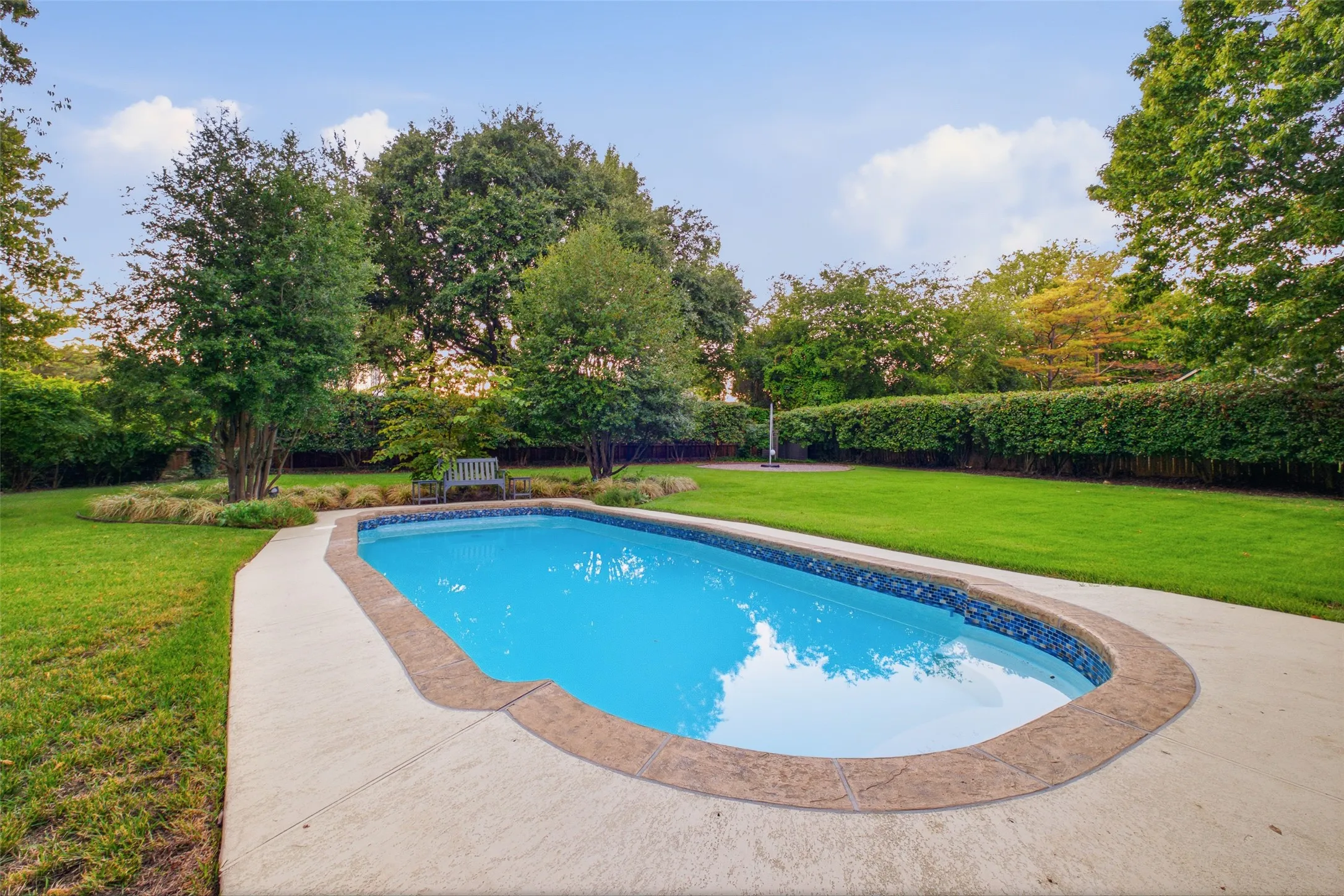 Sparkling pool with blue tile accents, surrounded by lush lawn and mature trees.