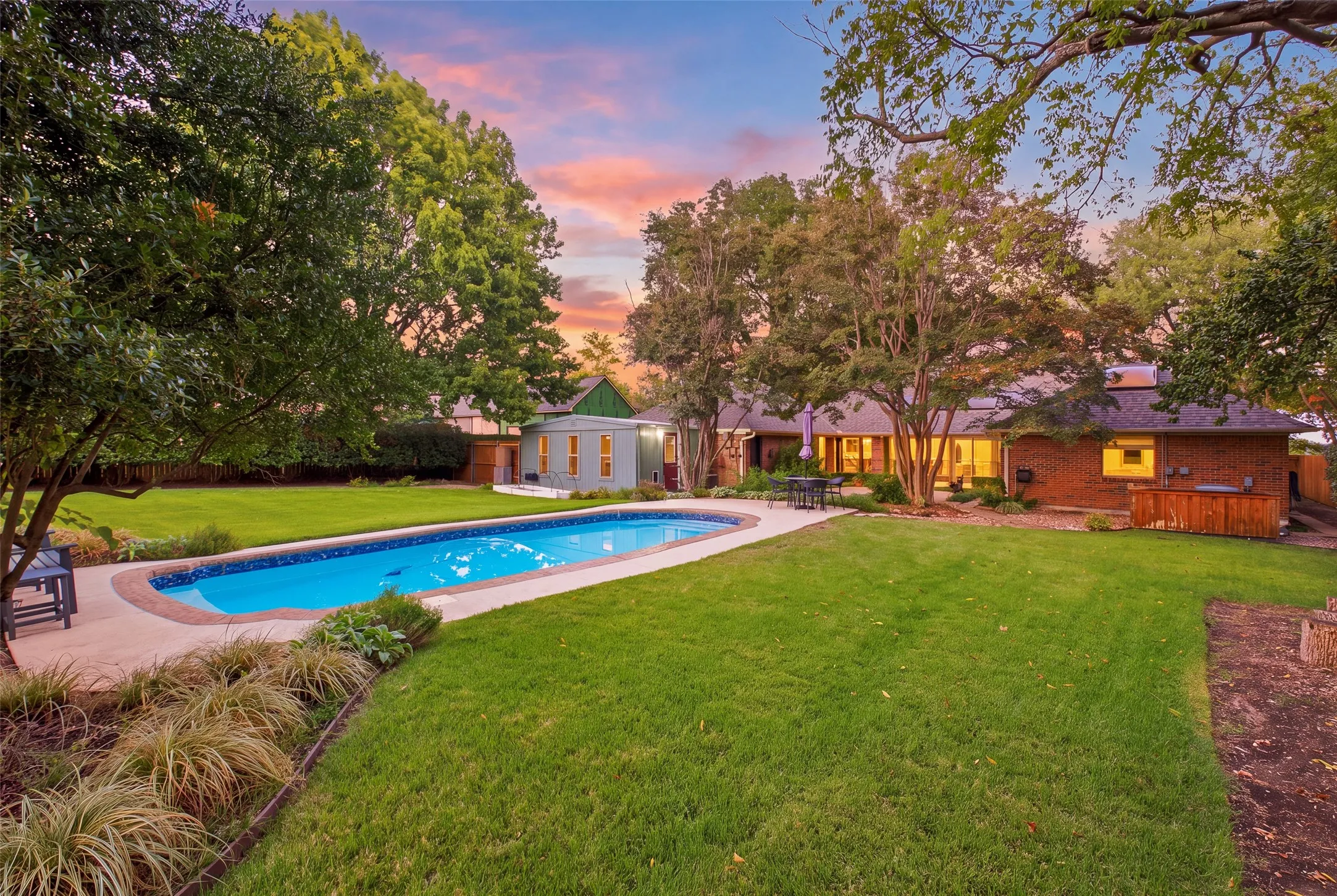 Golden hour at the pool, with the home and studio glowing beyond the lawn.