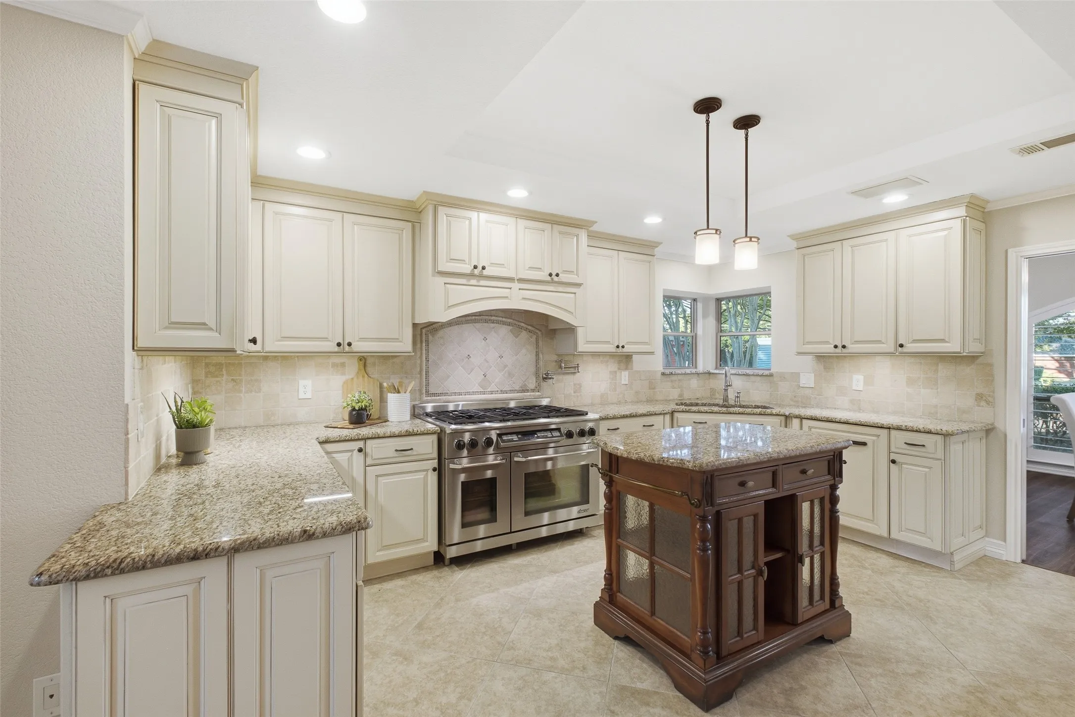 Chef's kitchen with granite counters, six-burner range with double ovens, pot filler and tile backsplash.
