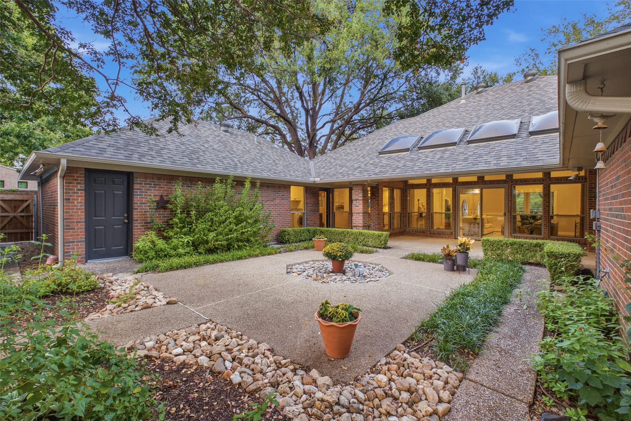 The home wraps the courtyard on three sides, with skylights and warm evening light at dusk.