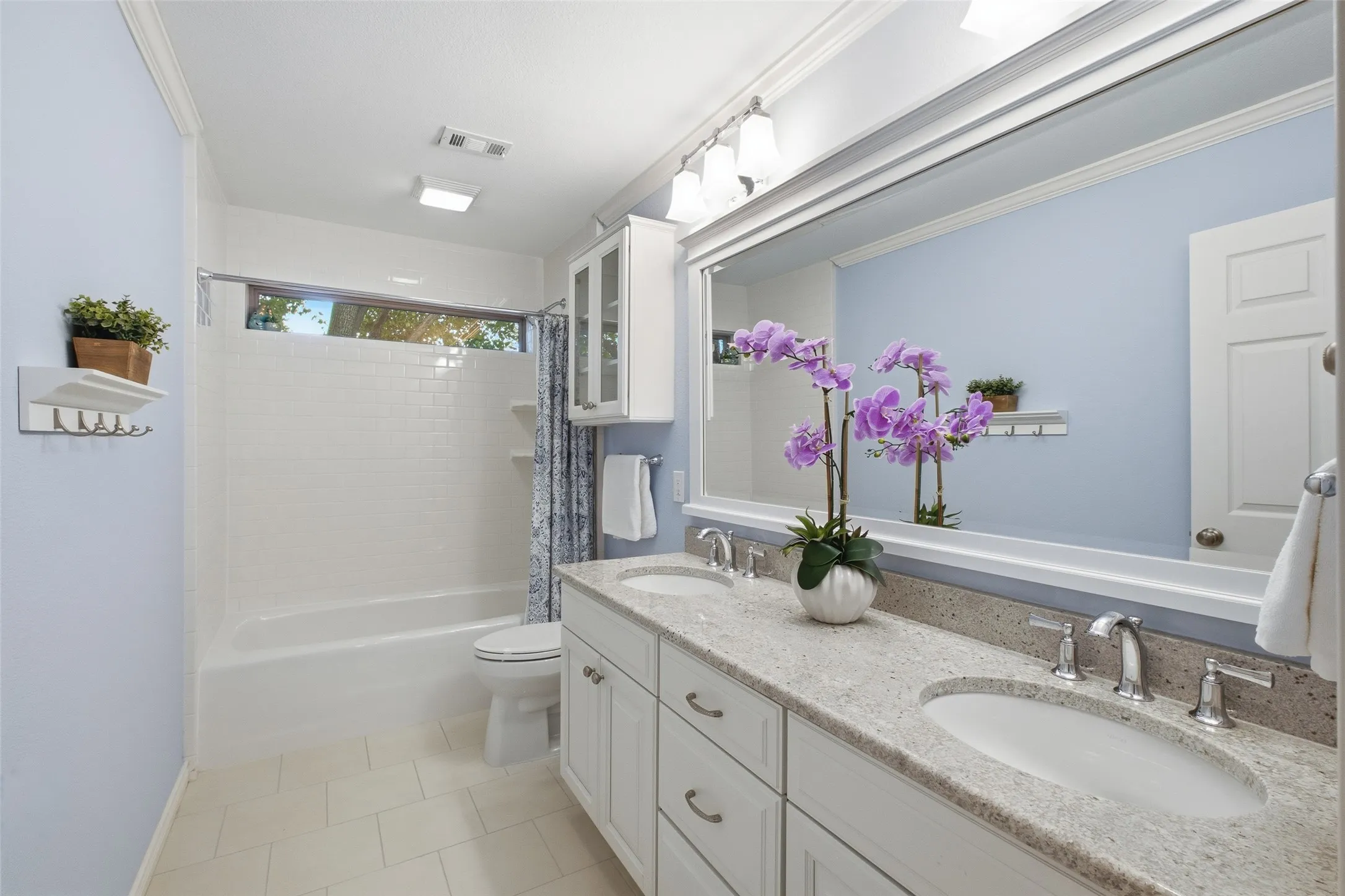 Hall bath with dual sinks, granite counters, subway-tile tub/shower and an oversized framed mirror.
