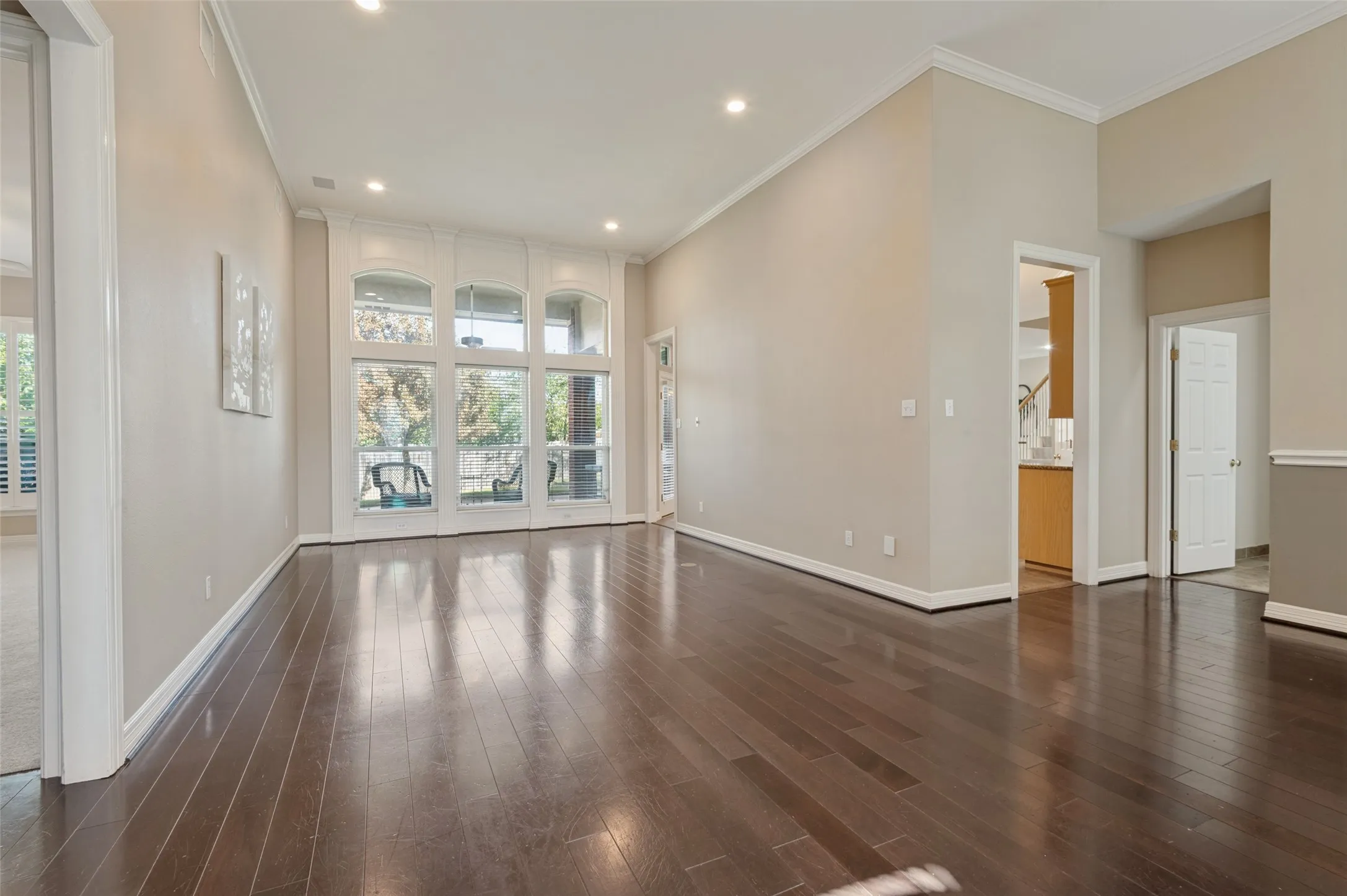 Open-concept living space featuring high ceilings, wood-finish flooring, recessed lighting, and expansive floor-to-ceiling windows with crown molding