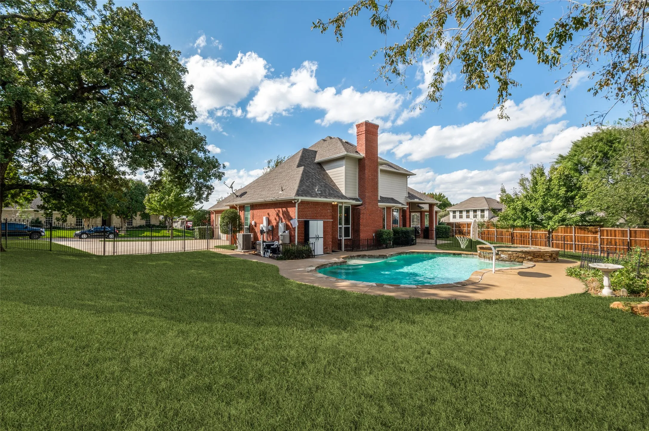 Rear exterior featuring a brick and siding facade, an expansive lawn, a built-in swimming pool with an attached spa, and a concrete patio