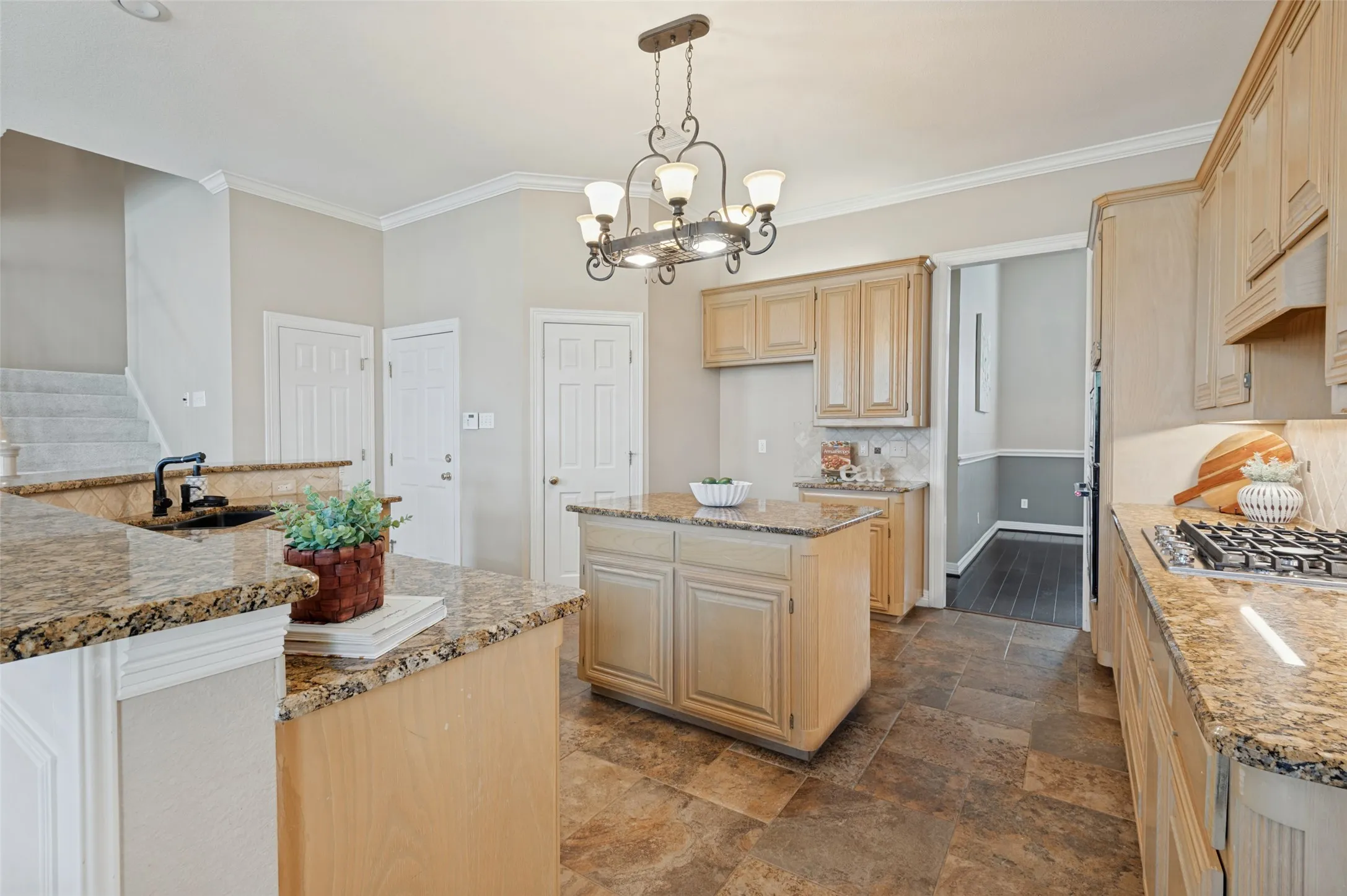 Kitchen featuring light wood cabinetry, stone-surface countertops, central island, decorative iron chandelier, and tile flooring