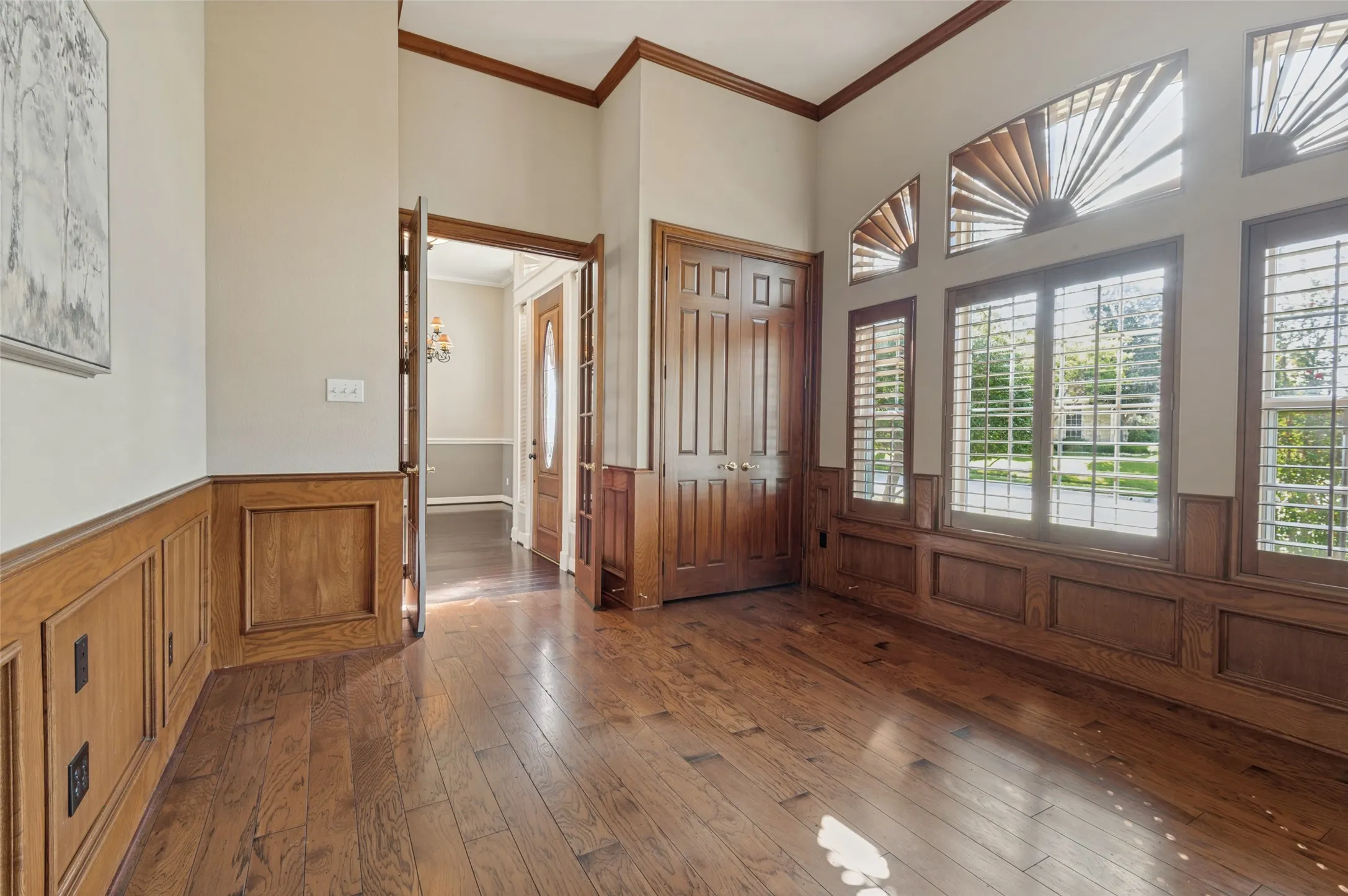 Wood-finish flooring, half-height wood wainscoting, multi-pane windows with sunburst transom detailing, and double-door storage cabinetry