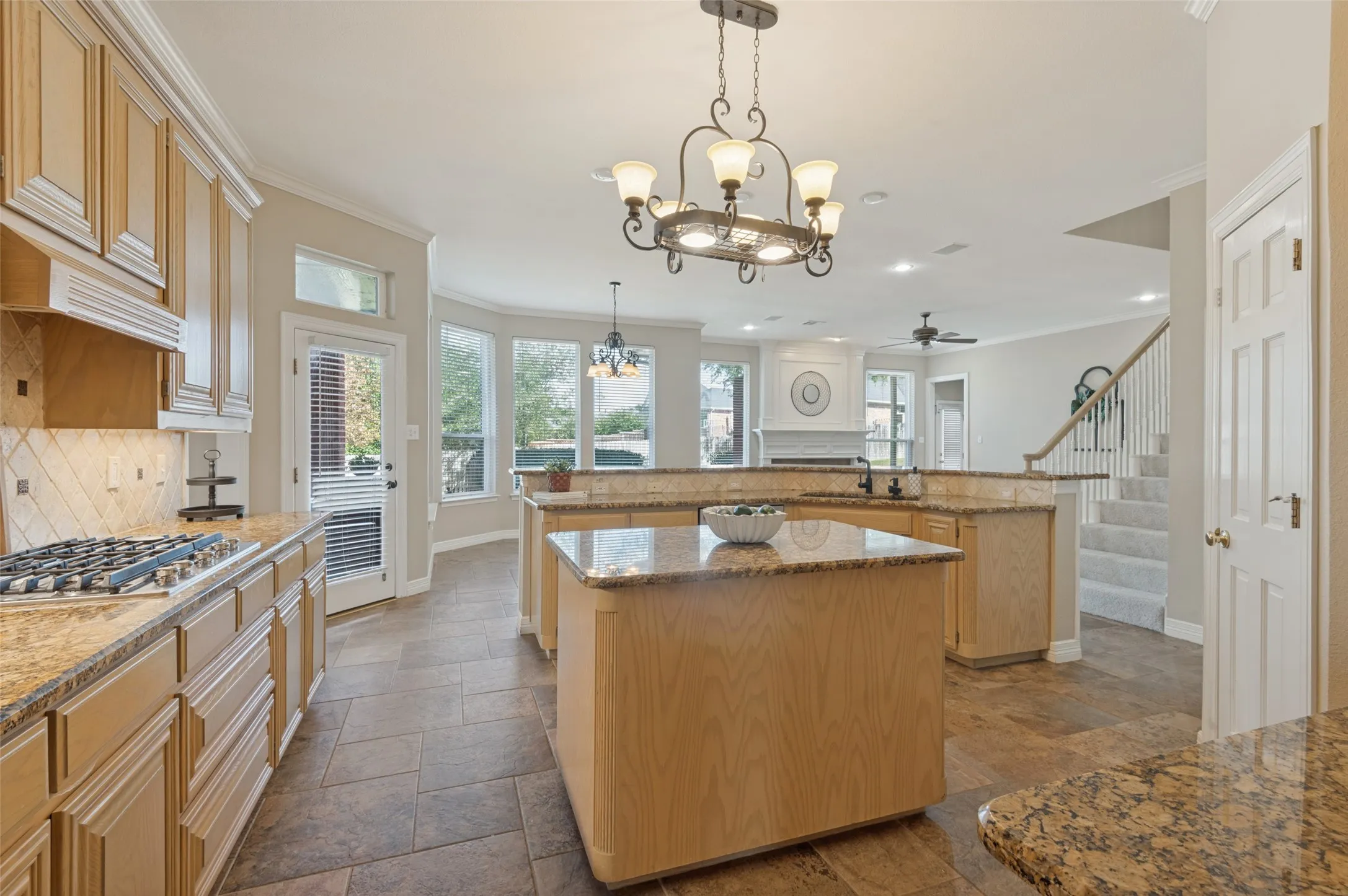 Kitchen featuring wood cabinetry, stone countertops, a central island, tile flooring, and decorative chandeliers