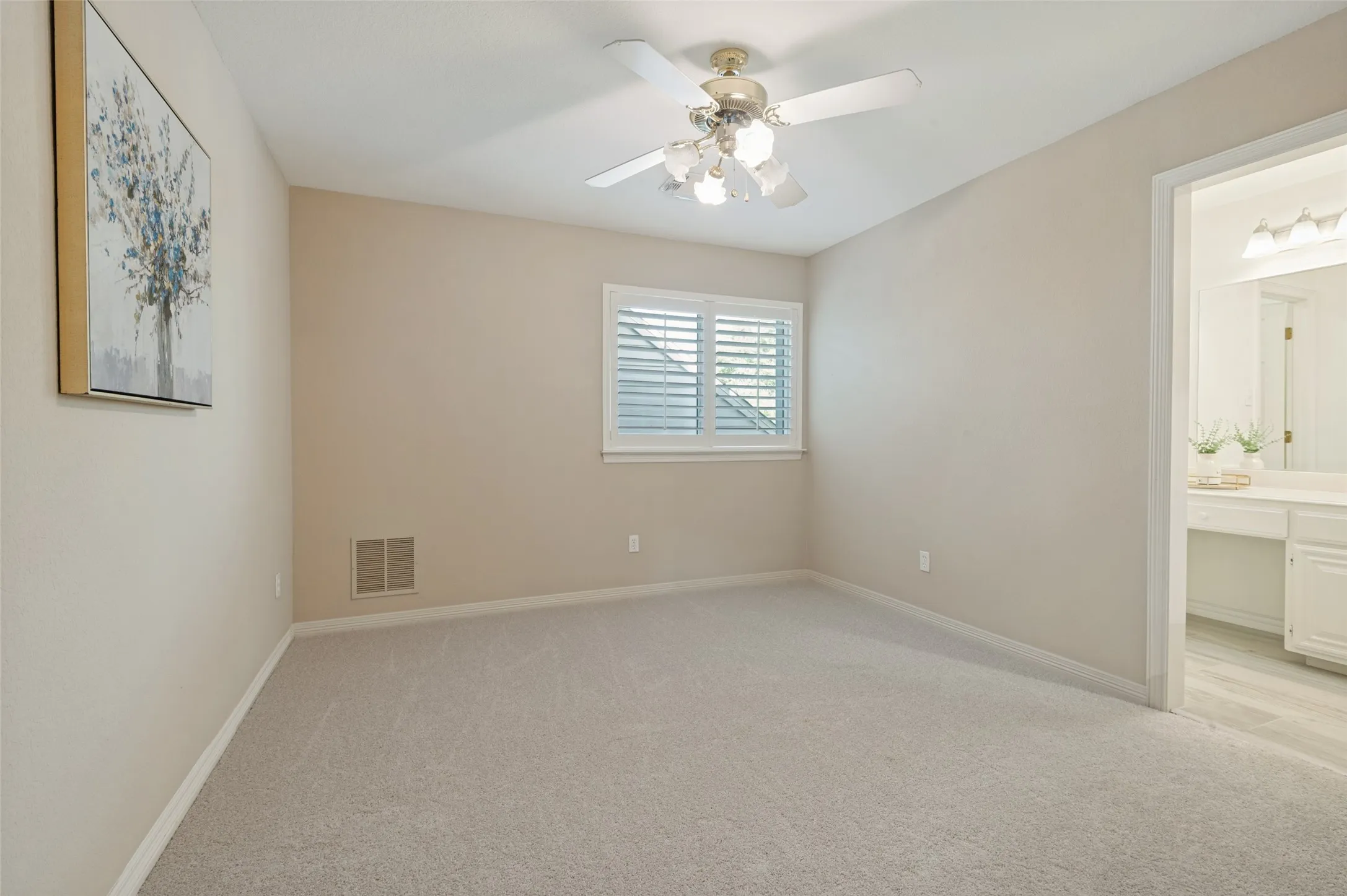 Neutral-toned interior space featuring wall-to-wall carpeting, an overhead ceiling fan with multi-light fixture, and plantation-style window shutters