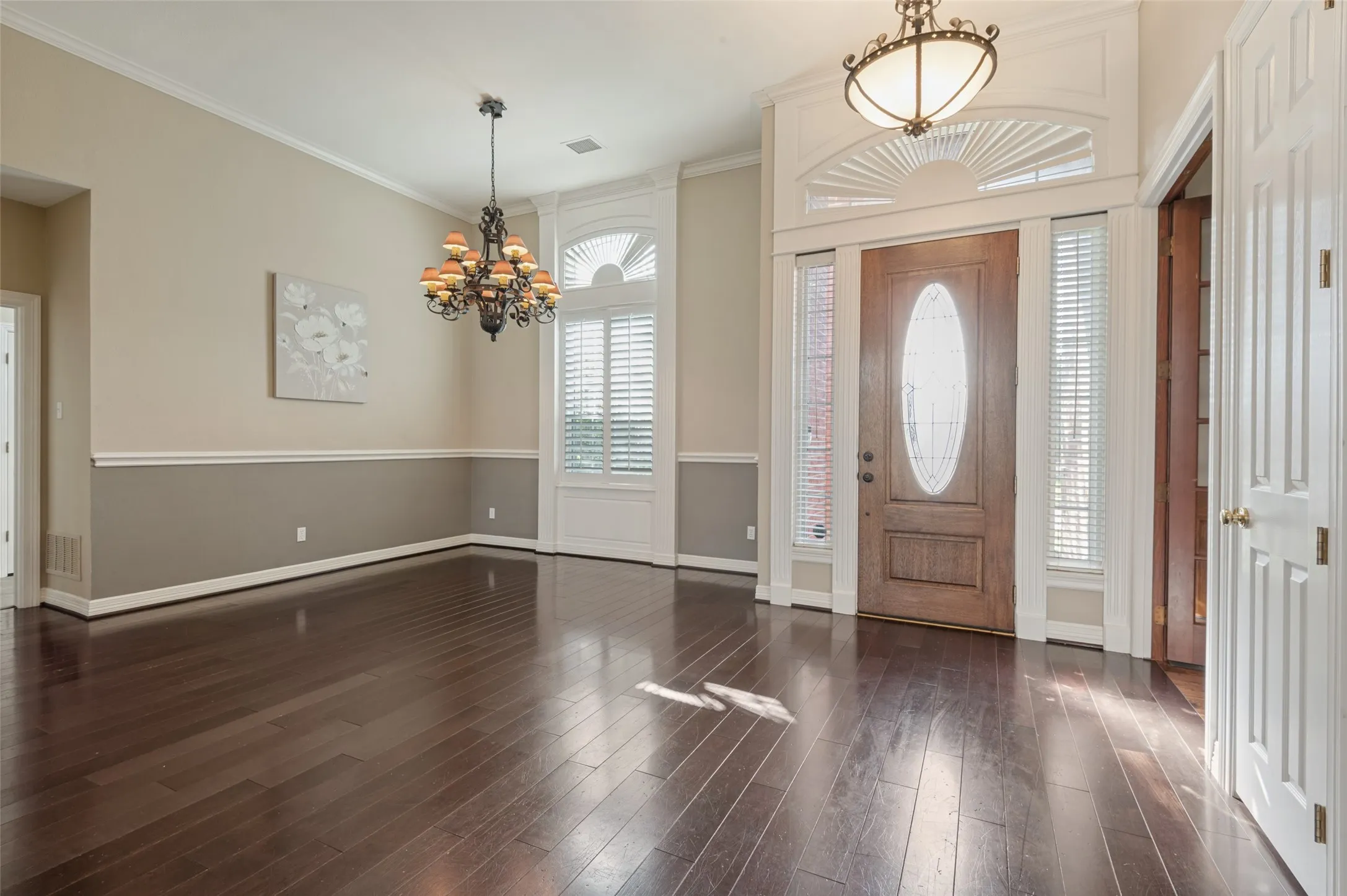 Entryway featuring wood-finish flooring, two-tone wall detailing, arched transom windows, iron chandelier, and a decorative glass-panel front door