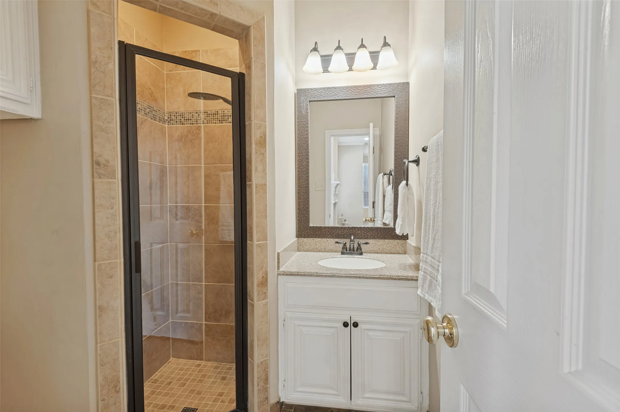 First floor bathroom  featuring a vanity with a light-tone stone countertop, an integrated oval basin, and a framed mirror