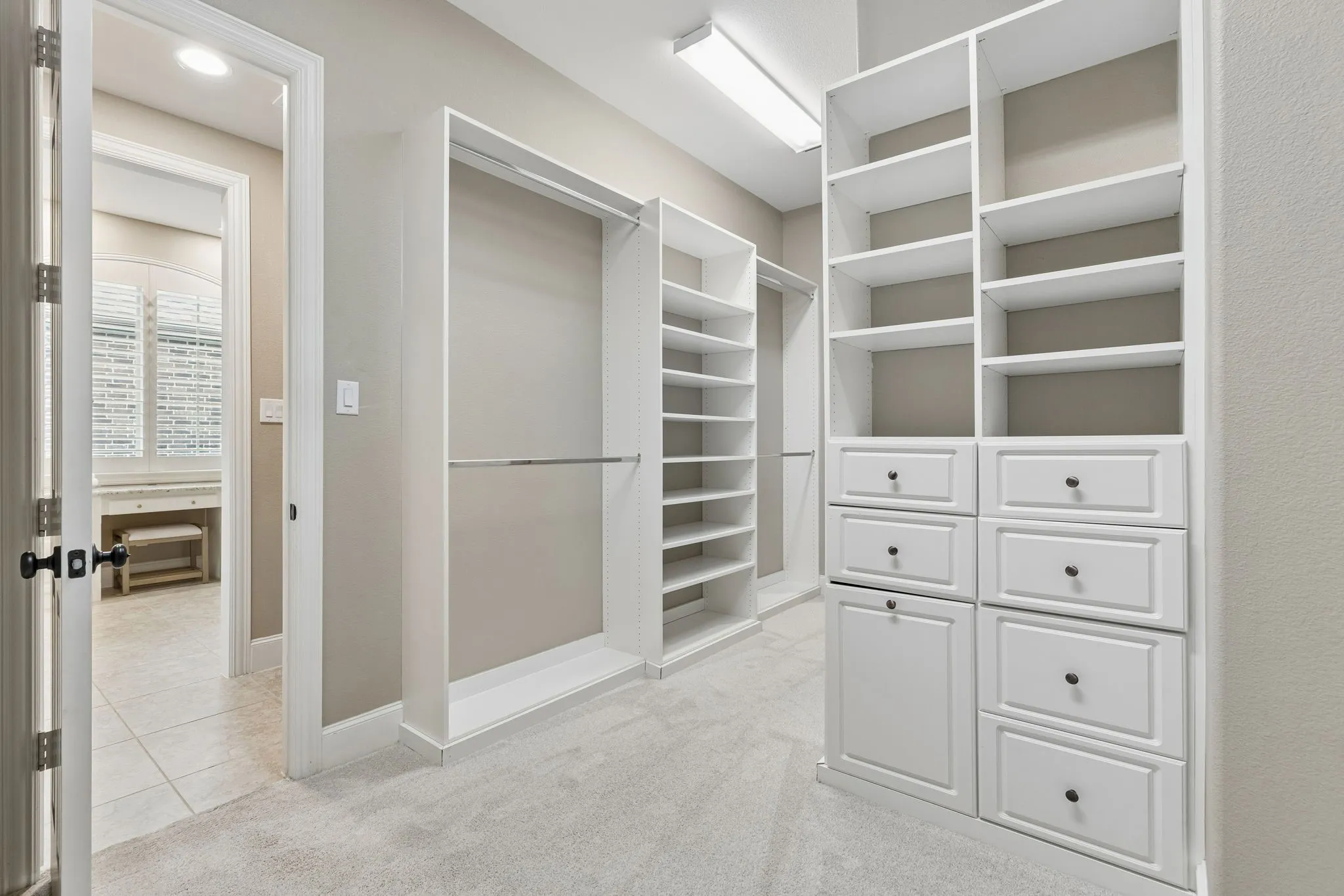 Walk-in closet featuring white built-in shelving, integrated dresser drawers, metal hanging rods, and neutral carpeting