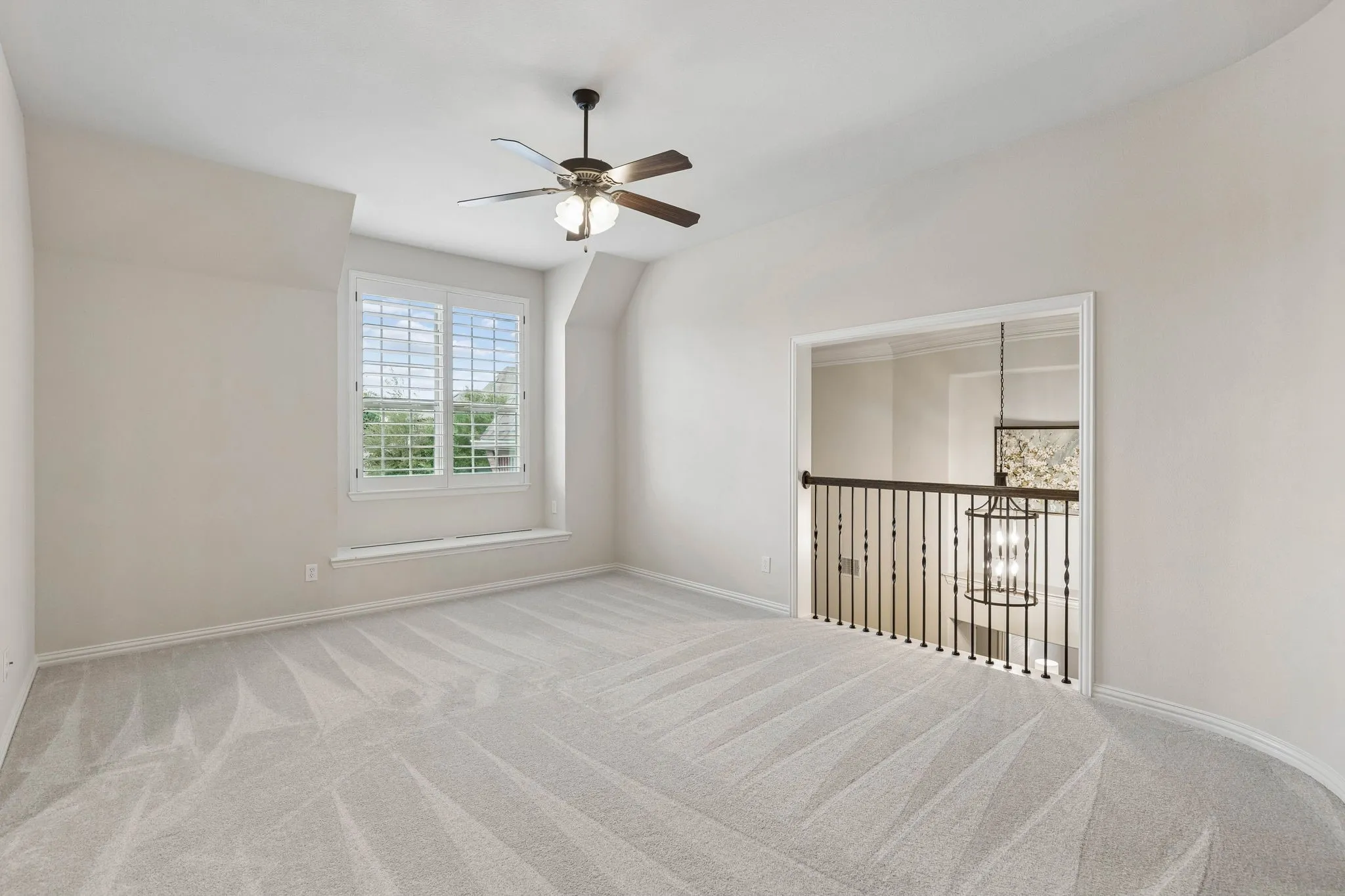 Carpeted room featuring a ceiling fan with integrated lighting, window shutters, a recessed window seat, and iron balusters